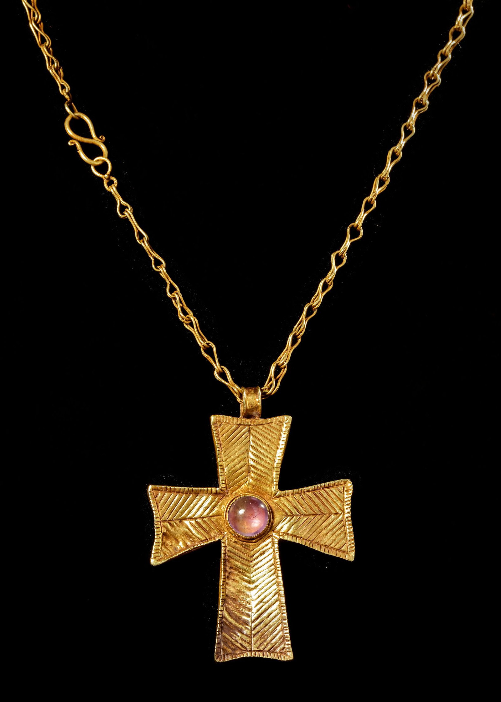 A LARGE PECTORAL CROSS IN PALE GOLD WITH A CHAIN, BYZANTINE, 6TH-7TH CENTURY AD: A large pectoral cross in pale gold/electrum. the cross is made from a robust sheet construction with identical striated decoration on both sides. At the centre there is a large cabochon amethyst whil