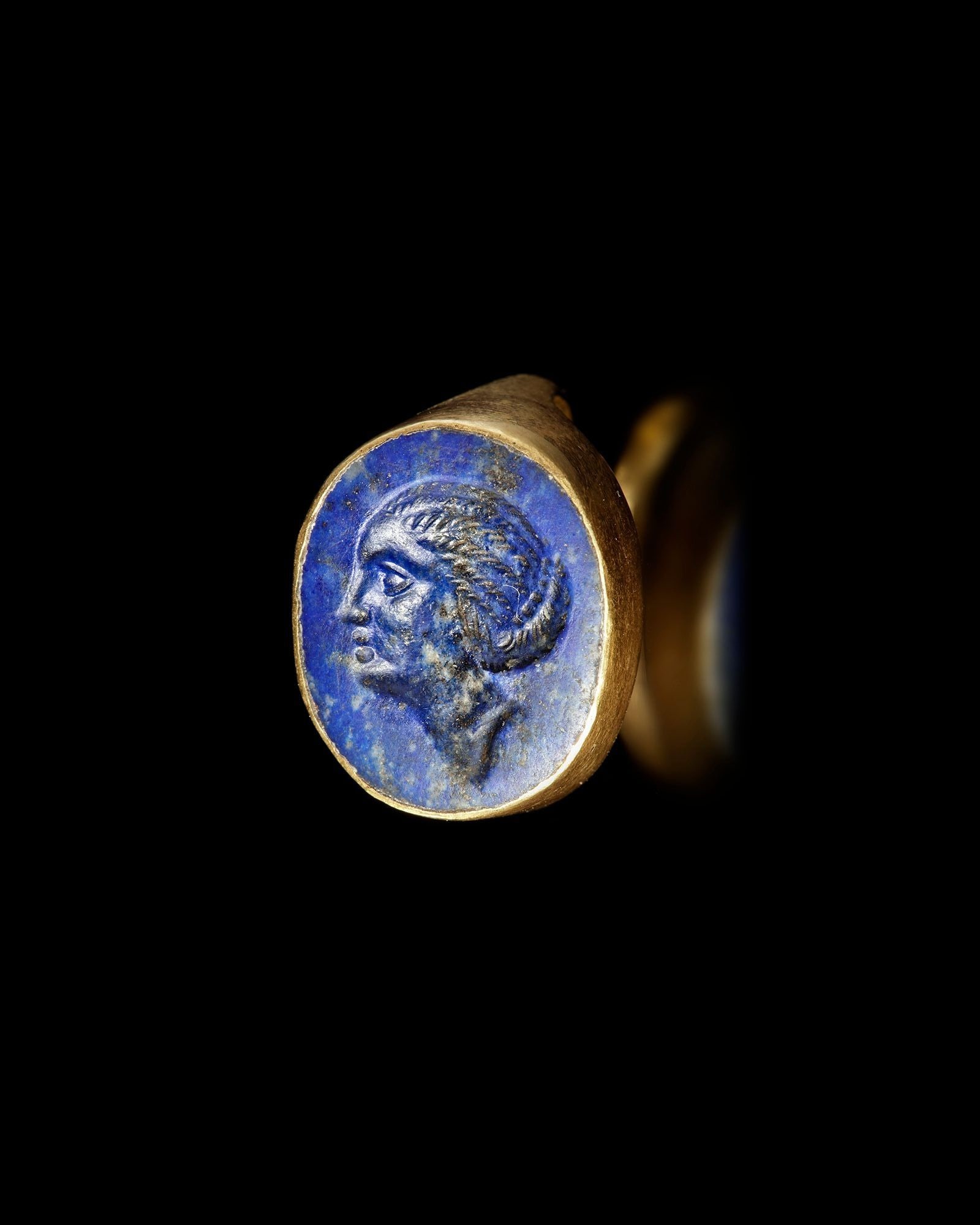 A PTOLEMAIC GOLD RING WITH LAPIS LAZULI INTAGLIO, 3RD-2ND CENTURY BC: Ptolemaic gold ring set with a deep-blue lapis lazuli intaglio portraying a Hellenistic royal woman, traditionally associated with Arsino?«. The sharply carved profile and rich color of the stone exe