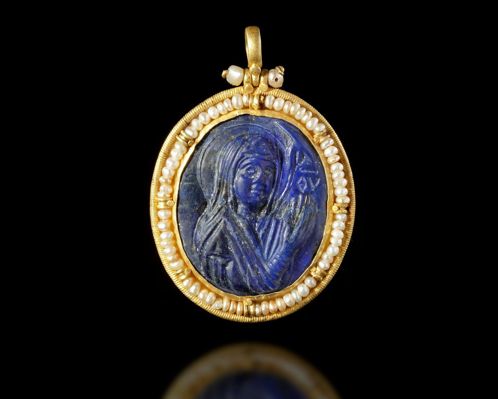 A BYZANTINE LAPIS LAZULI CAMEO PENDANT OF THE VIRGIN MARY 12TH-15TH CENTURY AD: Byzantine or early medieval lapis lazuli cameo pendant depicting the Virgin Mary, finely set within a gold frame adorned with delicate pearls.The reverse features a carved cross. 4.5 by 3.6 cm.