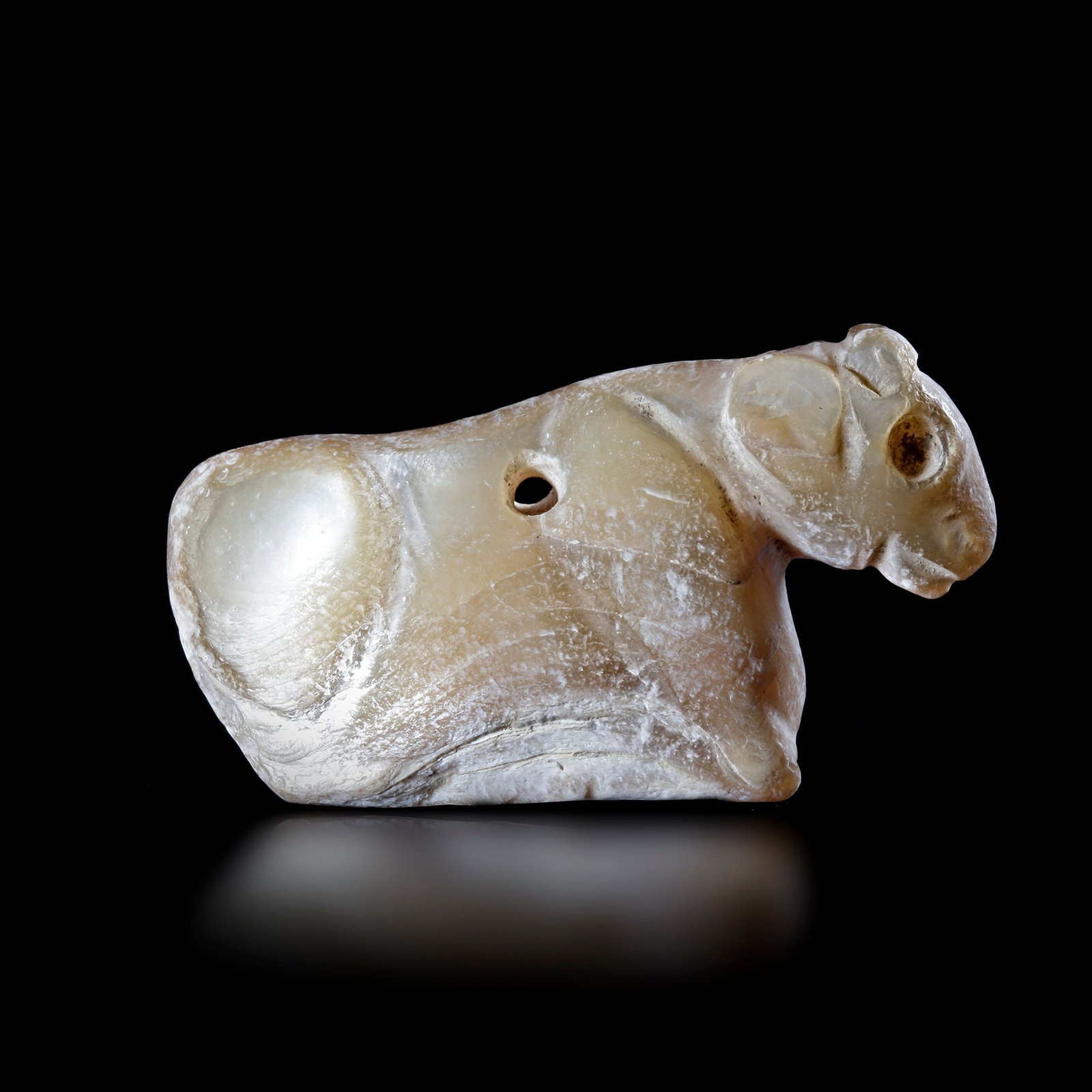AN AMULET IN SHELL IN THE SHAPE OF A RECLINING BOVINE, NEAR EAST, 3RD MILLENNIUM BC: An amulet in the shape of a reclining bovine in shell.4.7 by 2.5 cm. 16.7 gr.