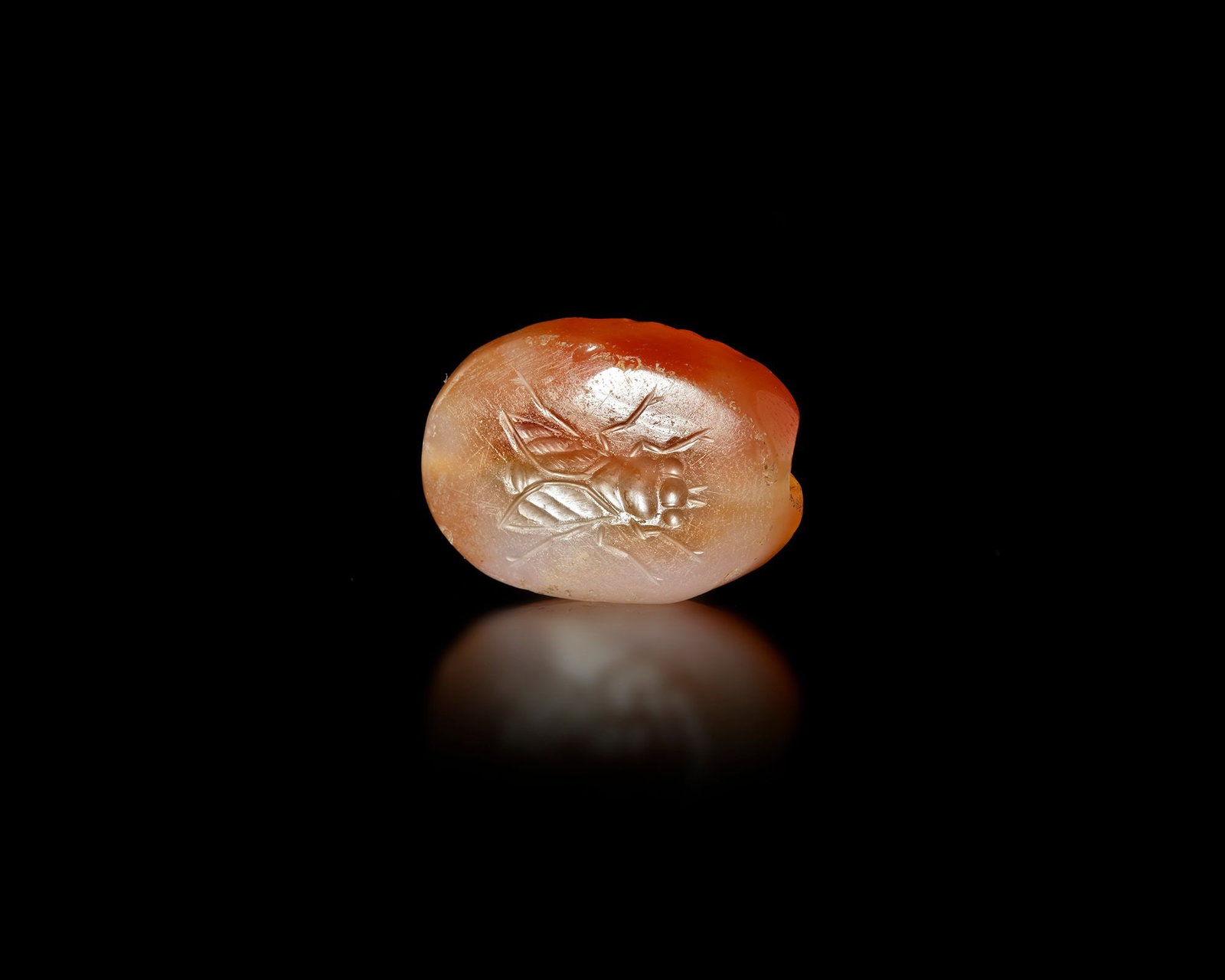 A GREEK CARNELIAN SCARABOID WITH FLY INTAGLIO, 4TH-3RD CENTURY BC: Greek orange carnelian scaraboid finely engraved with the image of a fly, a motif associated with realism and everyday life in Classical glyptic art. Its smooth, rounded form and detailed carving refl
