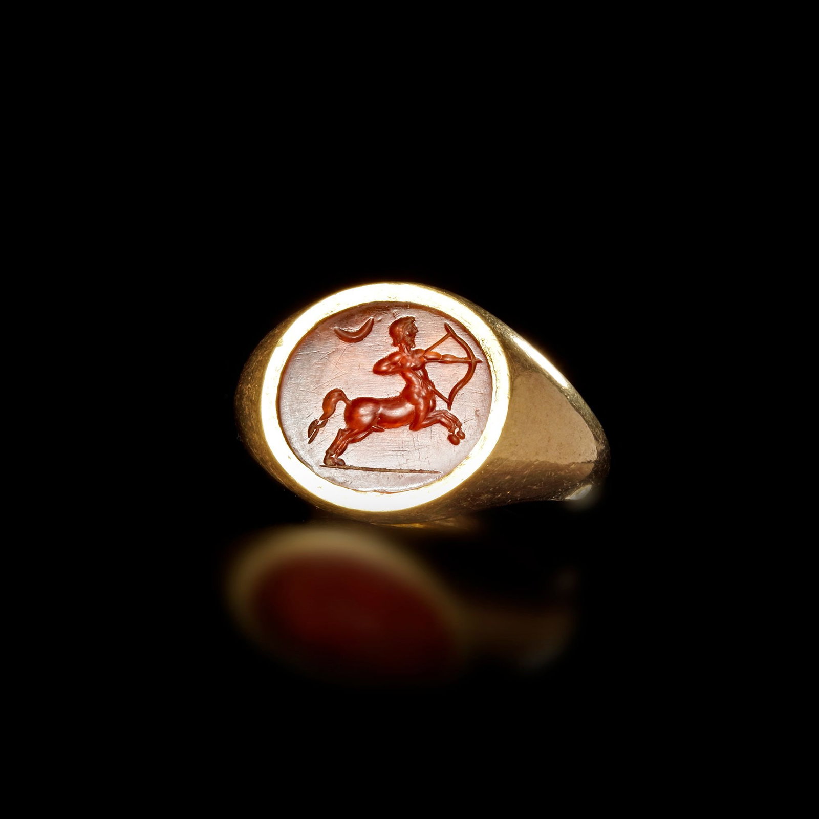 ROMAN GOLD RING WITH ORANGE INTAGLIO OF A HUNTING CENTAUR 1STâ€“2ND CENTURY A.D.: This powerful Roman gold ring features a vivid orange intaglio carved with the dynamic image of a centaurâ€”half man, half horseâ€”poised in mid-motion as he draws his bow bene