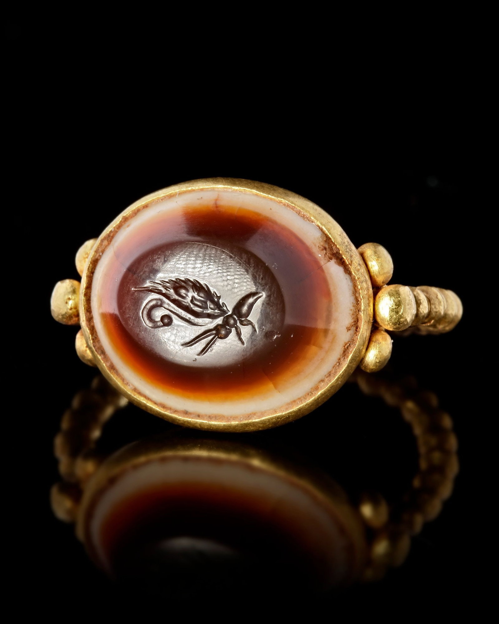 A LARGE ROMAN GOLD RING WITH AN INTAGLIO SHOWING A BUTTERFLY, 1ST CENTURY AD: A large Roman gold ring made from a heavy beaded gold wire, attached to a large beaten sheet gold bezel which holds an agate intaglio of a butterfly which represents Psyche, the soul in antiquity. Gol