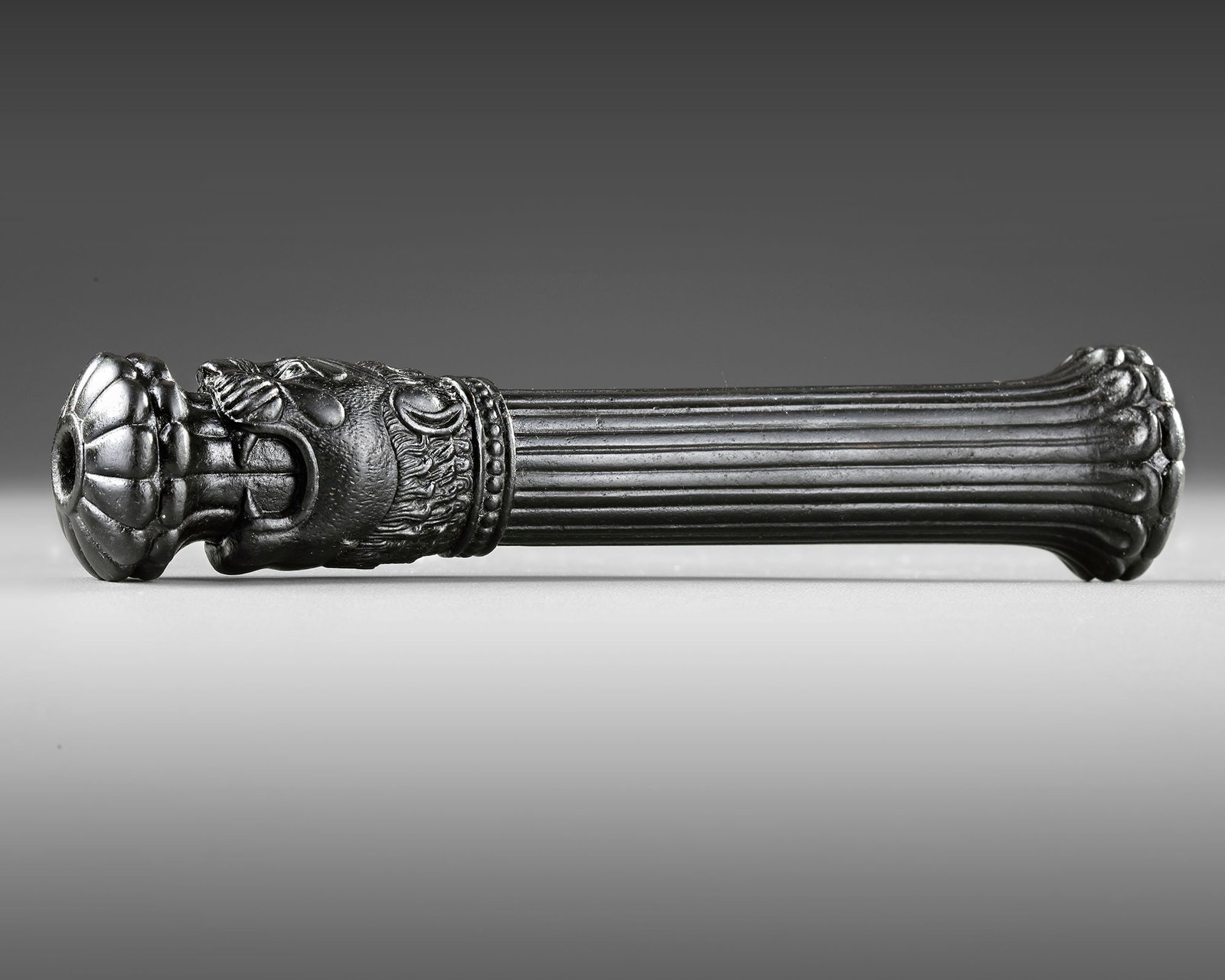 A BLACK STONE SCEPTRE FROM THE ACHAEMENID EMPIRE, 5TH CENTURY BC: An Achaemenid basalt cylindrical sceptre with a lion's head finial spouting a lotus flower from its mouth. The shaft of the sceptre is grooved and expands to a rounded base which itself is divided int