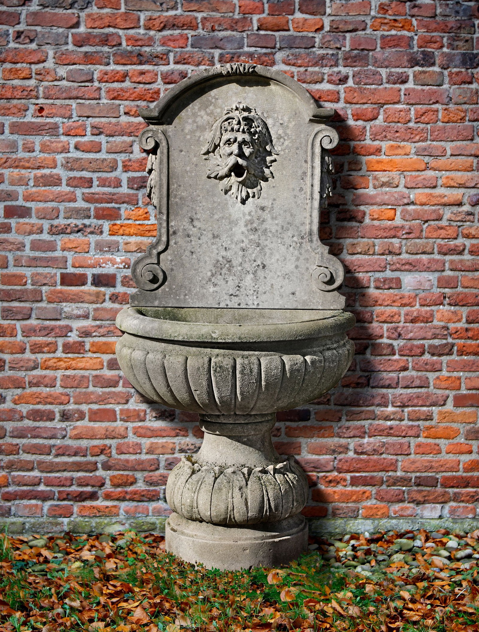 A CONTINENTAL SCULPTED LIMESTONE WALL FOUNTAIN, 20TH CENTURY: The arched reserve panel carved with a bearded man, his lips agape for the issuing water. Height 143 cm. Width 70 cm. Depth 40 cm.