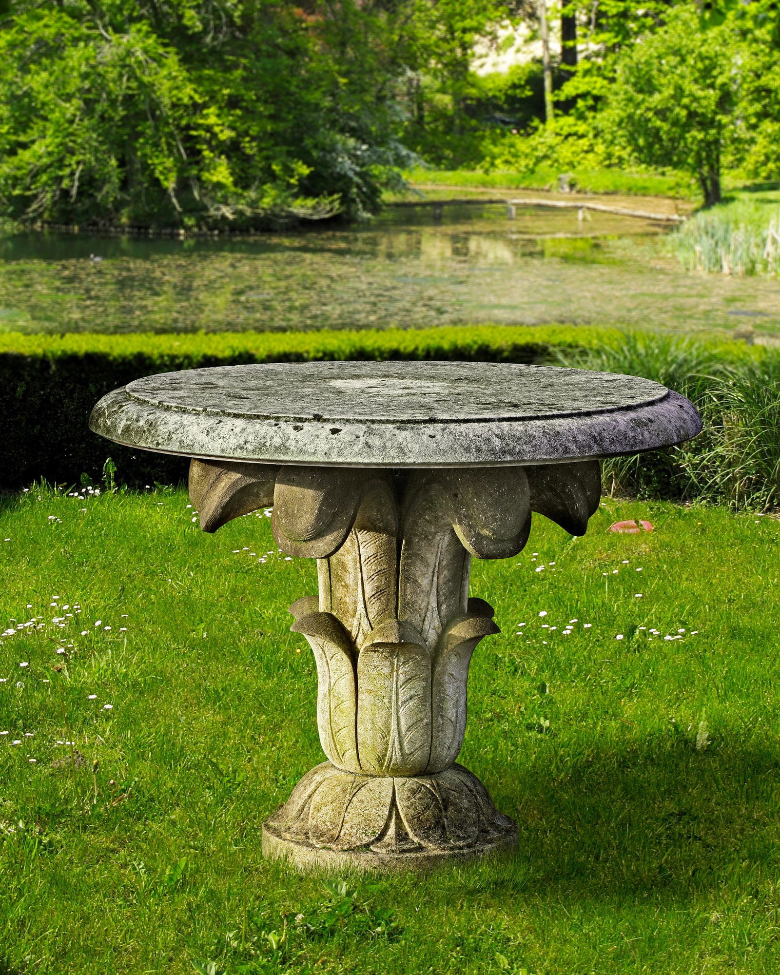A CARVED LIMESTONE GARDEN TABLE IN THE EARLY 19TH CENTURY STYLE, SECOND HALF 20TH CENTURY: The circular top supported on 6 folded leaves issuing from the stem, with lappet vase and spread foot. Height 80 cm. Diameter 105 cm.