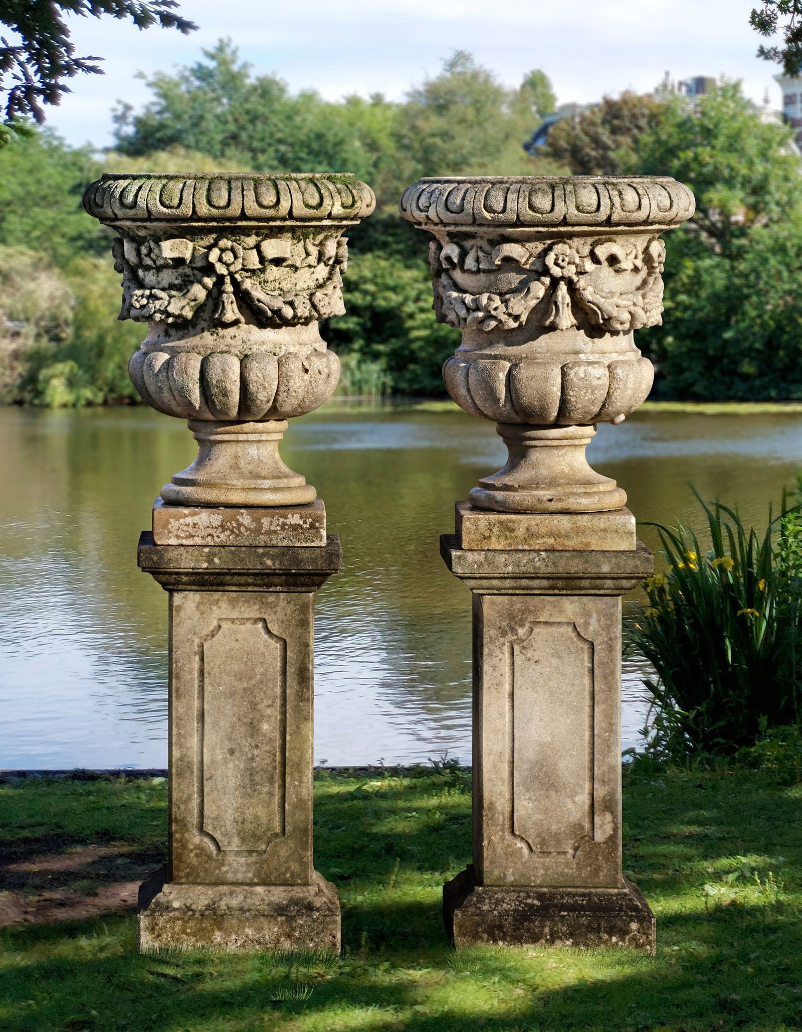 A PAIR OF CARVED LIMESTONE GARDEN URNS, LATE 19TH CENTURY: Atop associated, later pedestals. Height each 78 cm. Square 38 cm. Height overall 148 cm.