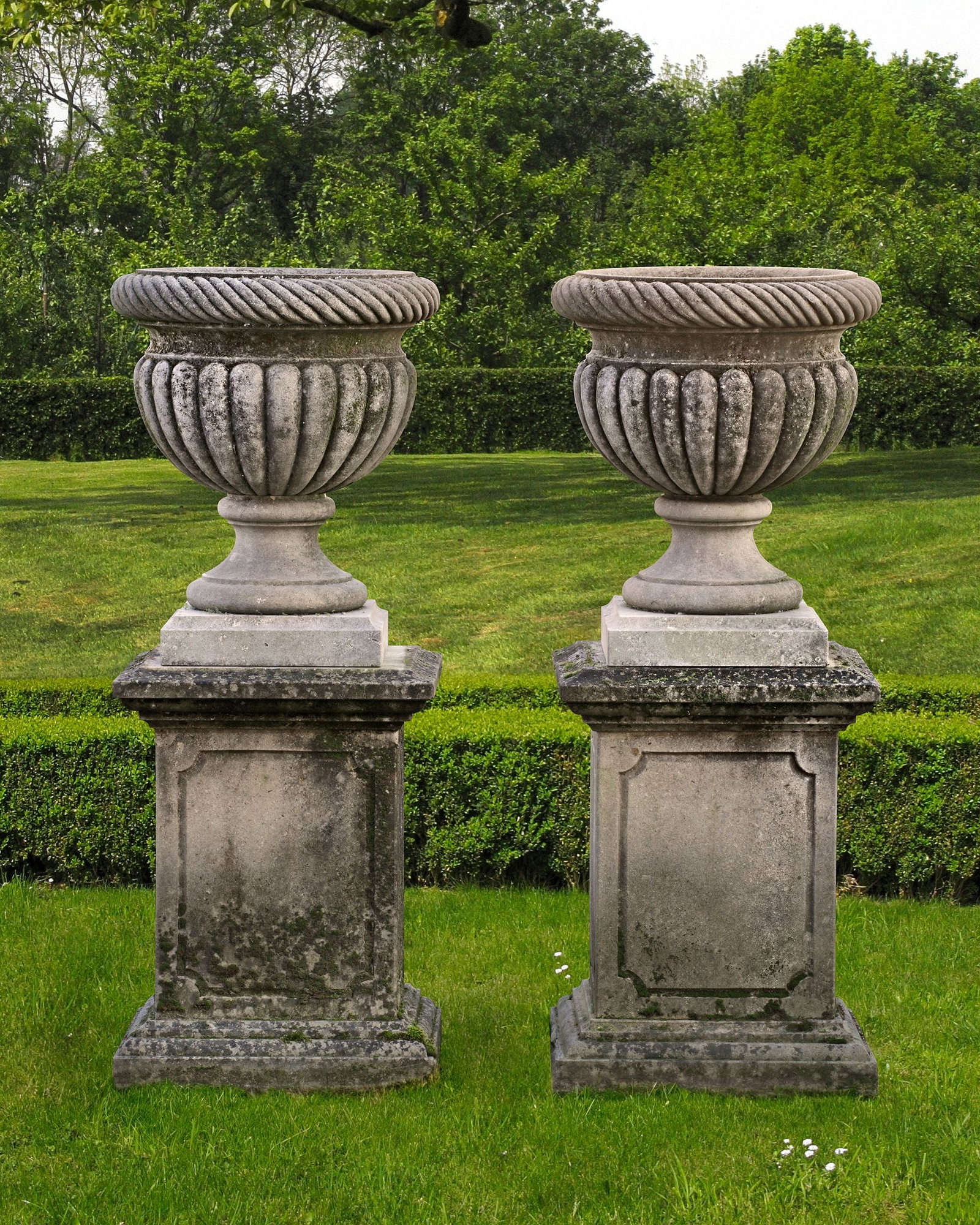 A PAIR CARVED LIMESTONE GARDEN URNS, 20TH CENTURY: Each with everted cable moulded rim above a semi-lobed body. Each atop a pedestal, 70 cm. high by 52 by 48 cm. high overall 135 cm.