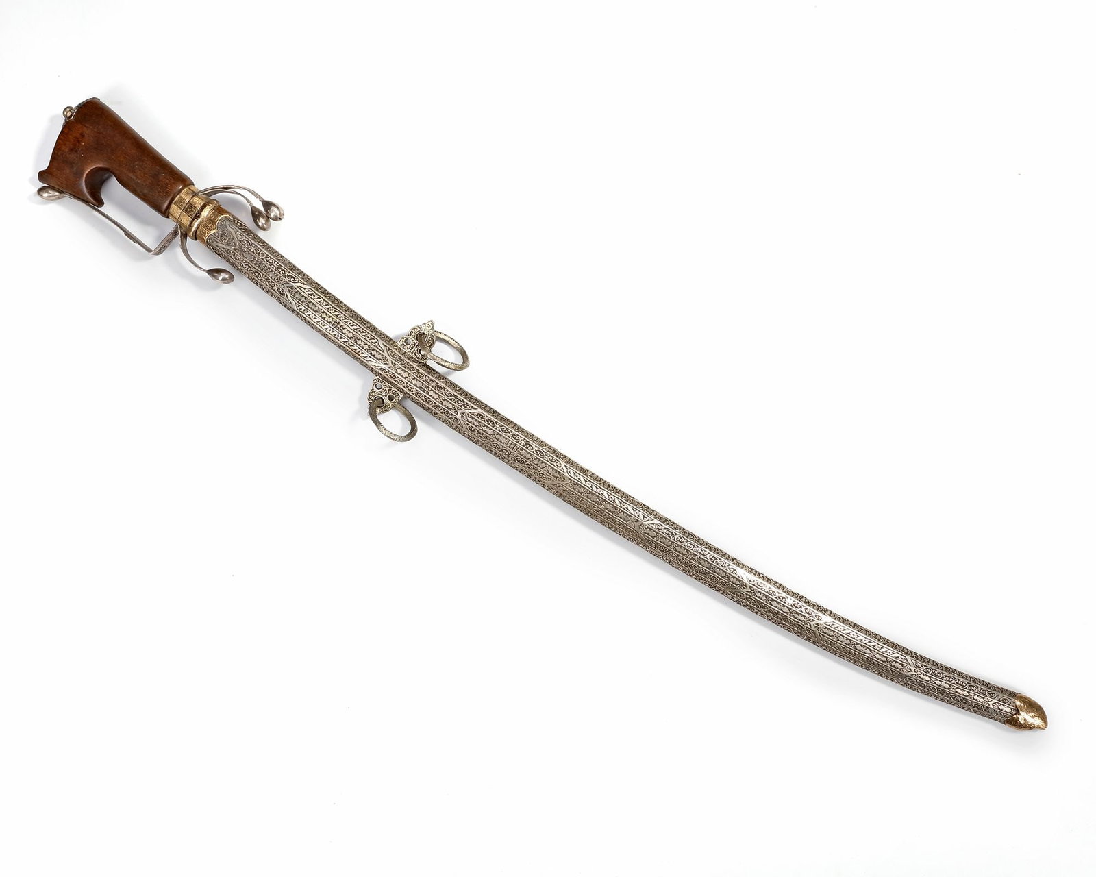 A SILVER SWORD, MOROCCO, 19TH CENTURY: A fine Moroccan sword with a wooden hilt and protective hand guard, richly adorned with engraved silver fittings. The long curved scabbard is decorated with intricate geometric and floral patterns, co