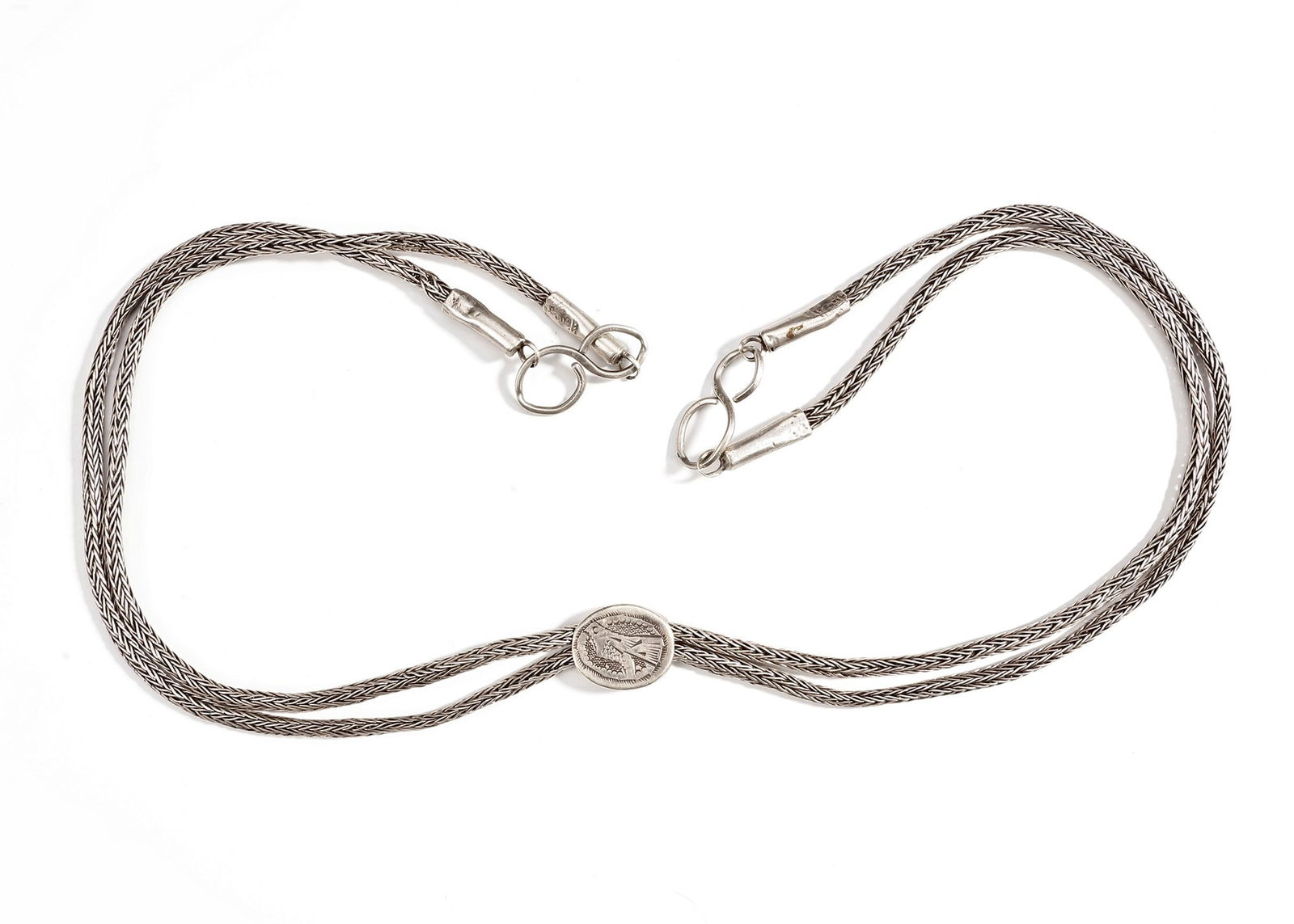 AN AFGHAN SILVER NECKLACE, 20TH CENTURY: A finely crafted Afghan silver necklace from the 20th century, featuring woven silver chains joined by an oval medallion engraved with a bird motif. ca. 72 cm. 102 gr. THE DR. SAAD AL-JADIR COLLECTION