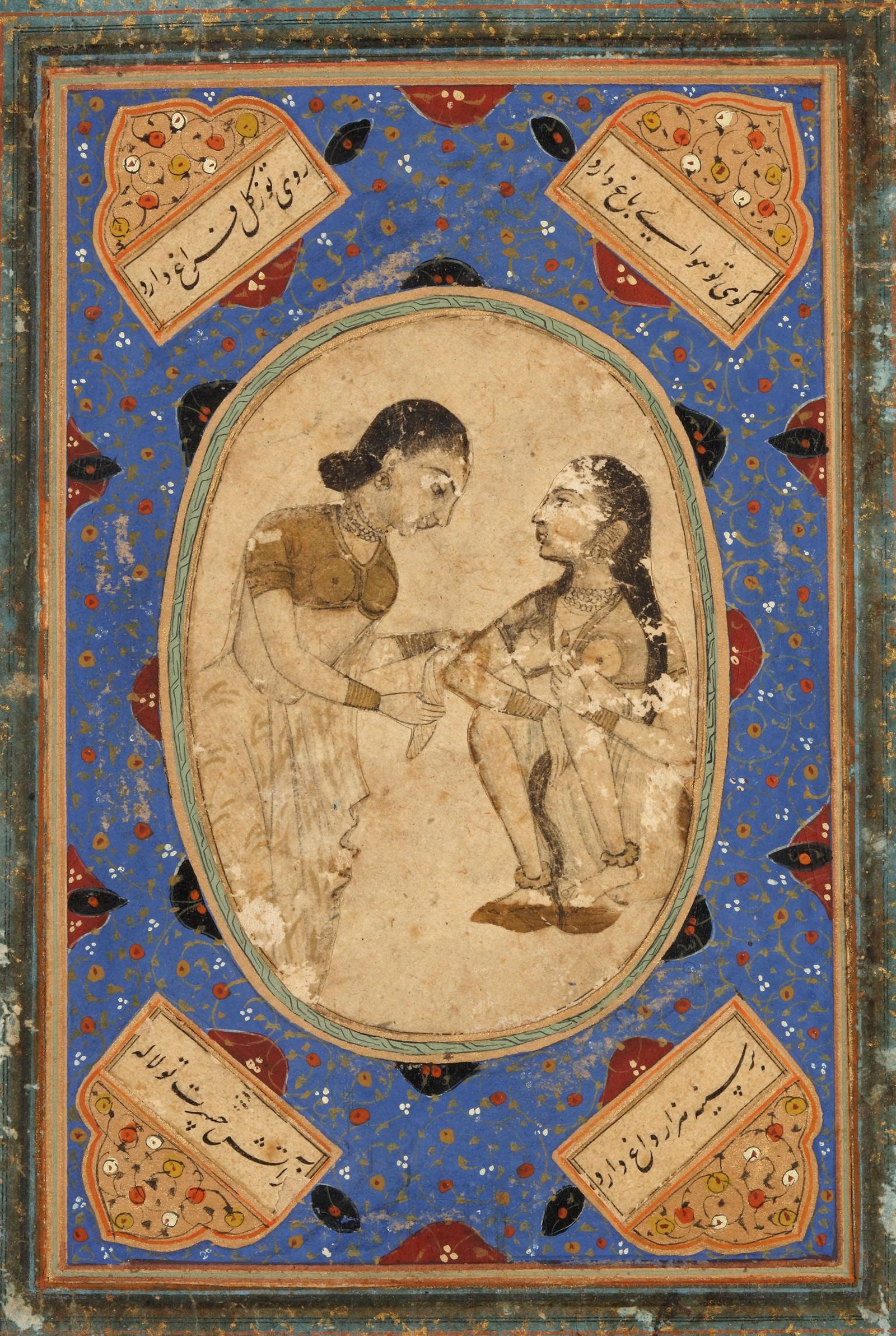 AN INTIMATE COURTLY SCENE, INDIA, 19TH CENTURY: Indian miniature painting showing two elegantly dressed women in a tender interaction within an oval medallion. Surrounded by a richly decorated blue border with floral motifs and calligraphy. 19.5 by