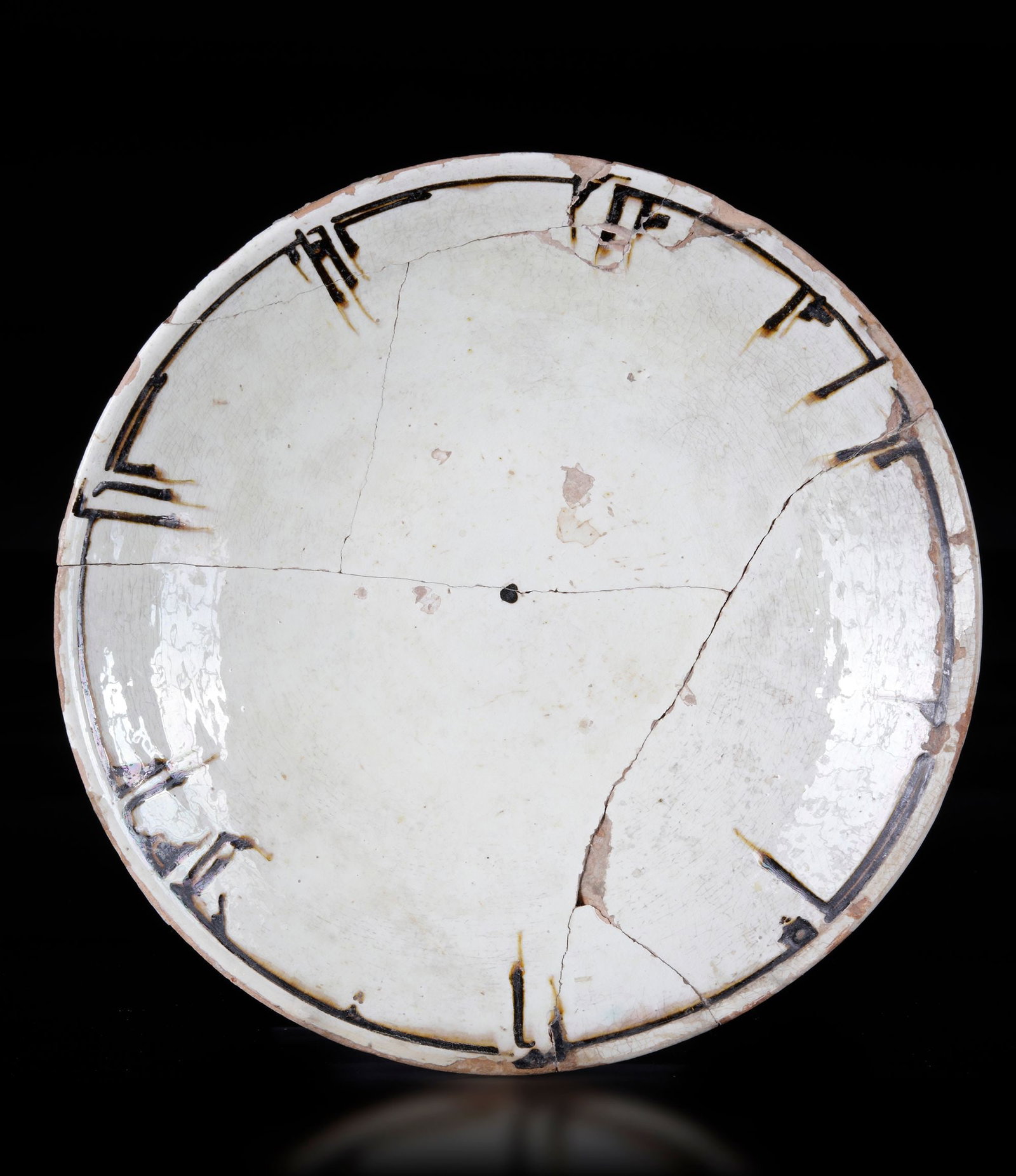 A SLIP-PAINTED POTTERY DISH, PERSIA, 10TH CENTURY: Of shallow rounded form on a short foot, decorated in manganese on a cream ground with a band of inscription to the rim. 24.5 cm. diam. Inscriptions: [al-ju]d min akhlaq ahl al-[ja]nnah..., 'Generosit