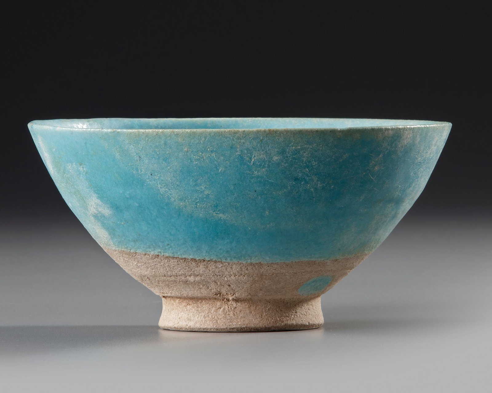A KASHAN TURQUOISE-GLAZED POTTERY BOWL, PERSIA 12TH-13TH CENTURY: A Persian pottery bowl with flaring body rising from straight foot, covered with a turquoise glaze stopping above the base to expose the buff ware. 7.5 by 15.5 cm.