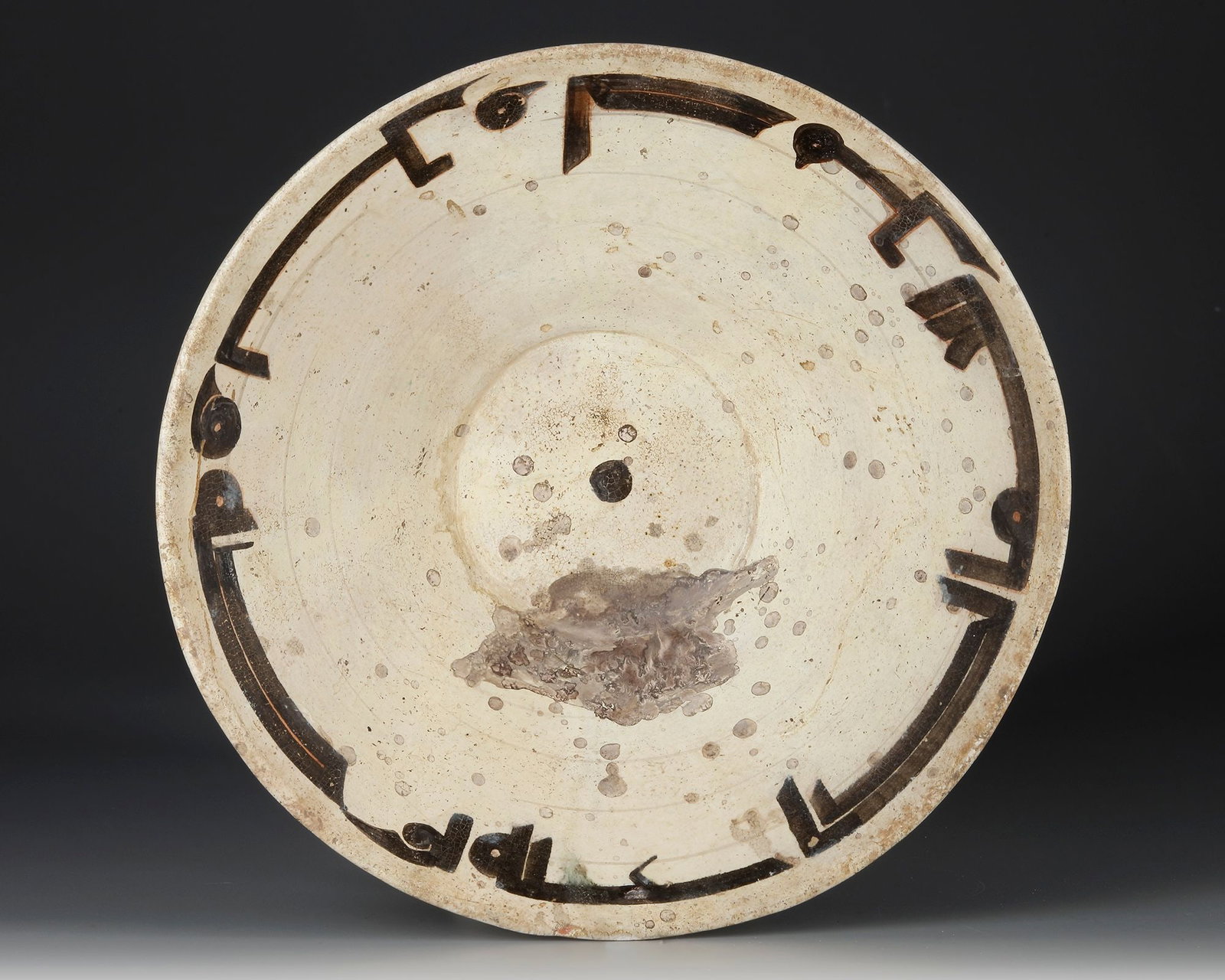 A LARGE SAMANID SLIP-PAINTED CALLIGRAPHIC POTTERY BOWL, NISHAPUR OR SAMARKAND 10TH CENTURY: Of broad, conical form rising from a short foot to a gently flaring rim, the bowl covered in a creamy white slip and decorated to the interior with a bold band of stylized Kufic calligraphy in dark br