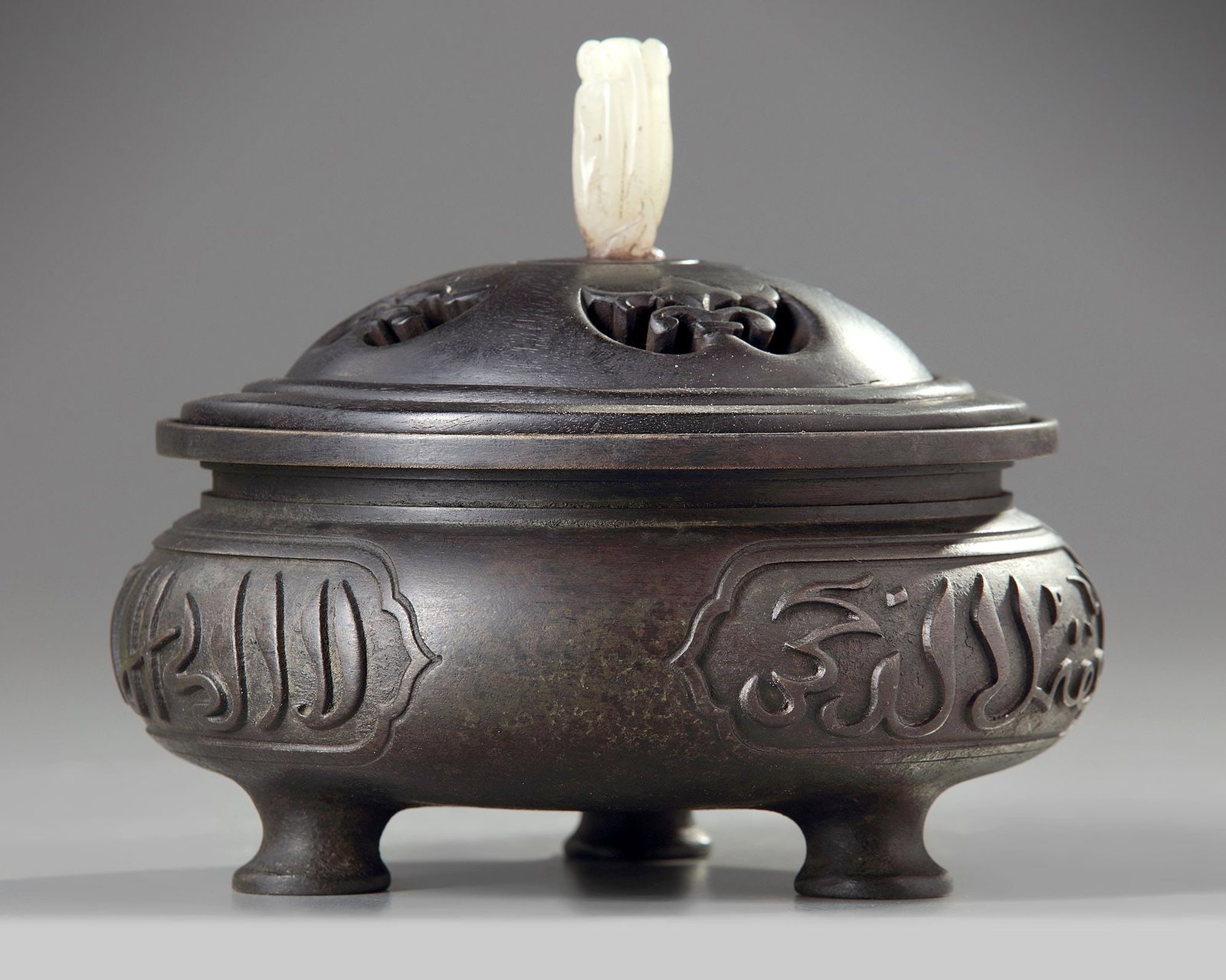 A CHINESE BRONZE TRIPOD CENSER FOR THE ISLAMIC MARKET, QING DYNASTY (1644-1911): Of a circular compressed body, raised on three feet with an everted rim, cast with three panels enclosing Arabic inscriptions. Height 7 cm. Diameter 14.5 cm. Weight 2.16 kg.