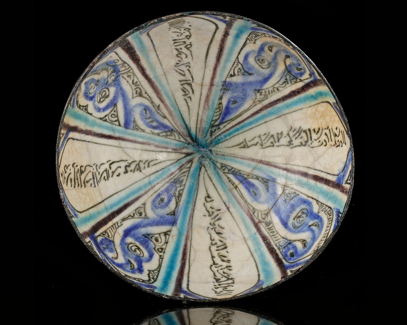 A KASHAN UNDERGLAZE-PAINTED POTTERY BOWL, PERSIA, 13TH CENTURY: Of deep rounded form on a short foot, decorated in cobalt-blue, turquoise and black on a white ground with radiating panels enclosing inscriptions and stylised vegetal motifs; the exterior with radiat