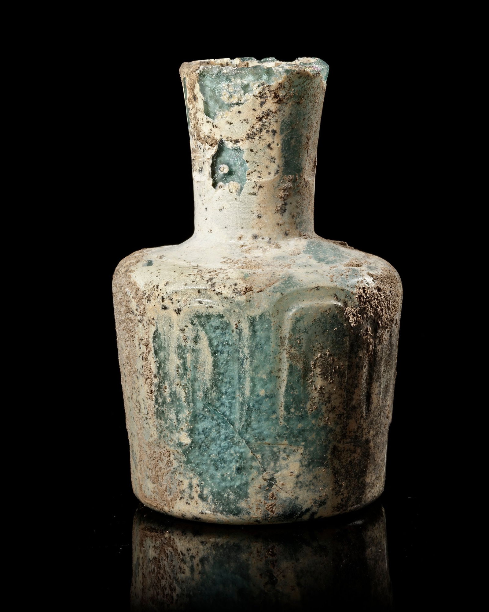A LIGHT LIME GREEN CUT GLASS BOTTLE, PERSIA, CIRCA 9TH CENTURY: With cylindrical body, flat shoulder and faceted tubular mouth, the body wheel-cut with panels of concentric oval designs divided by raised vertical ribs, iridescence on highlights. High. 11 cm.
