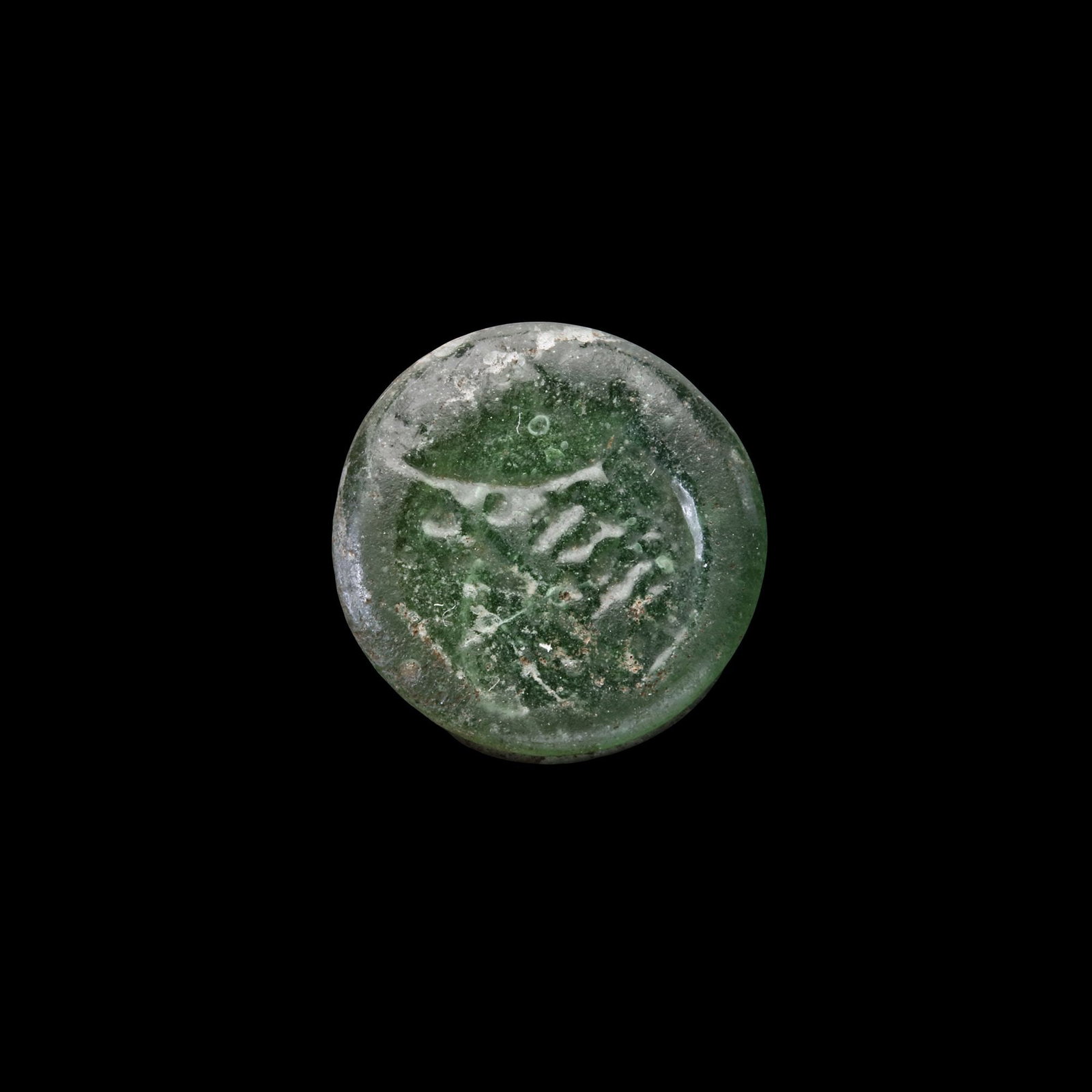 AN EARLY ISLAMIC GLASS WEIGHT OF HALF DIRHAM: Glass weight, moulded and stamped, transparent dark-green in colour, citing in the centre with the name Al-Zahir (412-427 AH/1021-1036 AD). 1.499 g., 14 mm. coin weight: half dirham, B 205-N 61