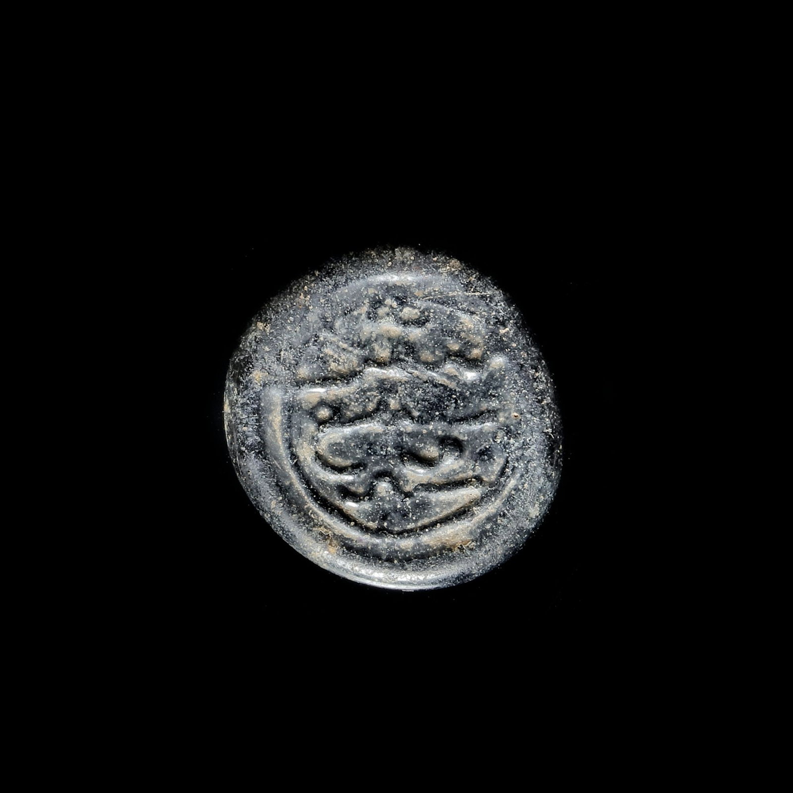 AN EARLY ISLAMIC GLASS WEIGHT OF DIRHAM, 13TH-14TH CENTURY: Glass weight, moulded and stamped, dark violet-black in colour, citing in the centre with " Al-Awdi, the year 67". 2,9 g., 20 mm. coin weight: dirham.