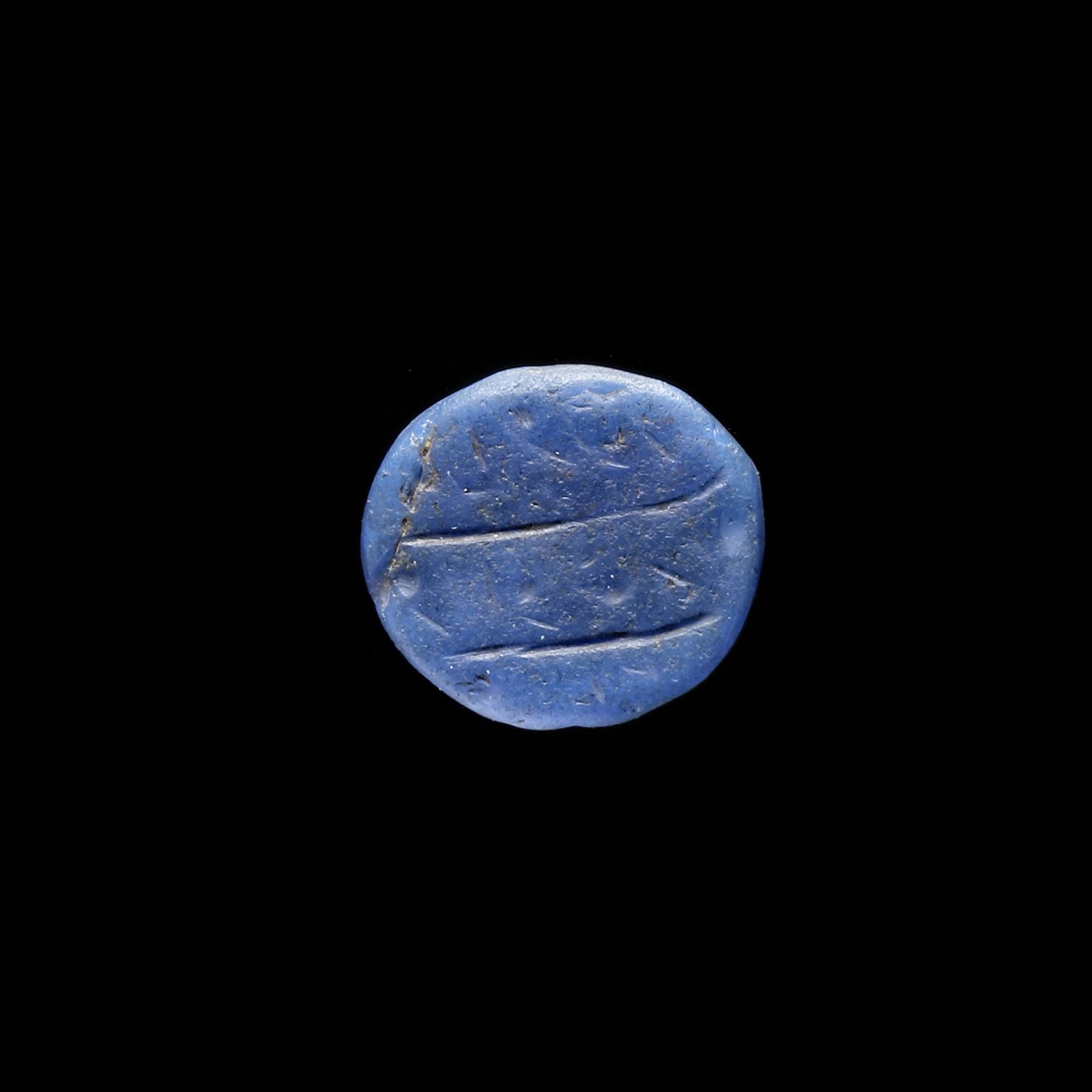 AN EARLY ISLAMIC GLASS WEIGHT OF QUARTER DIRHAM, 10TH-11TH CENTURY: Glass weight, moulded and stamped, opaque blue in colour, citing in the centre with 2 lines of undeciphered Arabic text. 0.941 g., 14 mm. coin weight: quarter dirham.