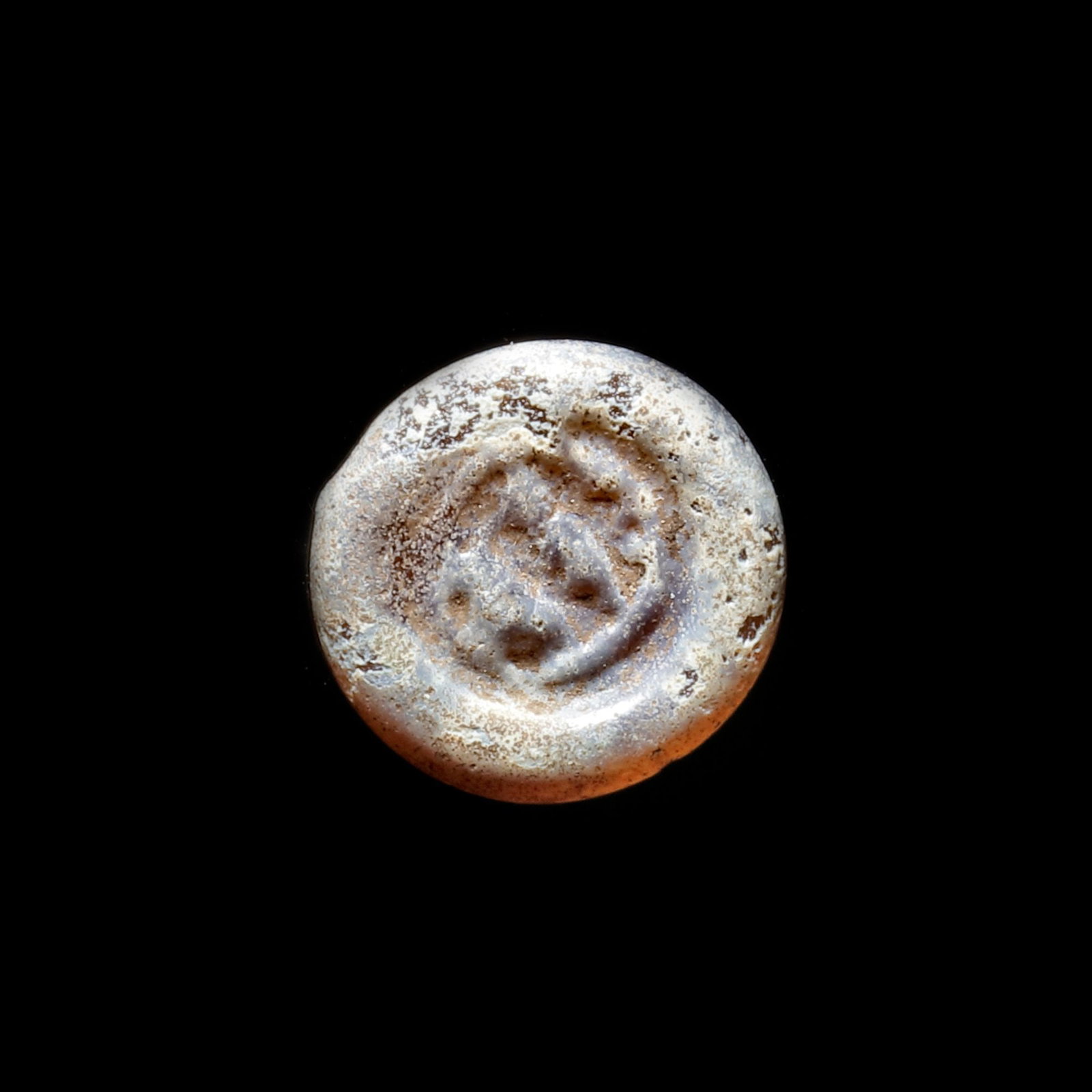 AN EARLY ISLAMIC GLASS WEIGHT OF HALF DIRHAM,10TH-11TH CENTURY: Glass weight, moulded and stamped, opaque brown in colour with white splashes, citing in the centre with 2 lines of undeciphered Arabic text. 1.479 g., 14 mm. coin weight: half dirham.