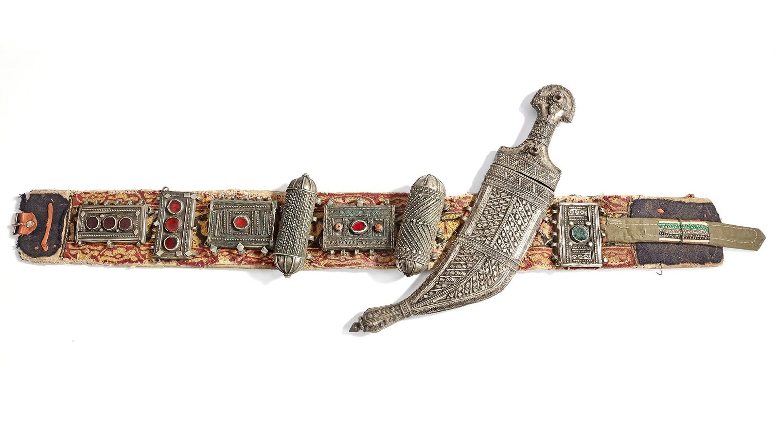 A SILVER DAGGER WITH BELT, YEMEN, 19TH CENTURY: A traditional Yemeni dagger (Jambiya) with an ornate silver hilt and scabbard, richly decorated in geometric patterns. The belt is embellished with silver mounts and colorful stones. 40 by 9 cm.
