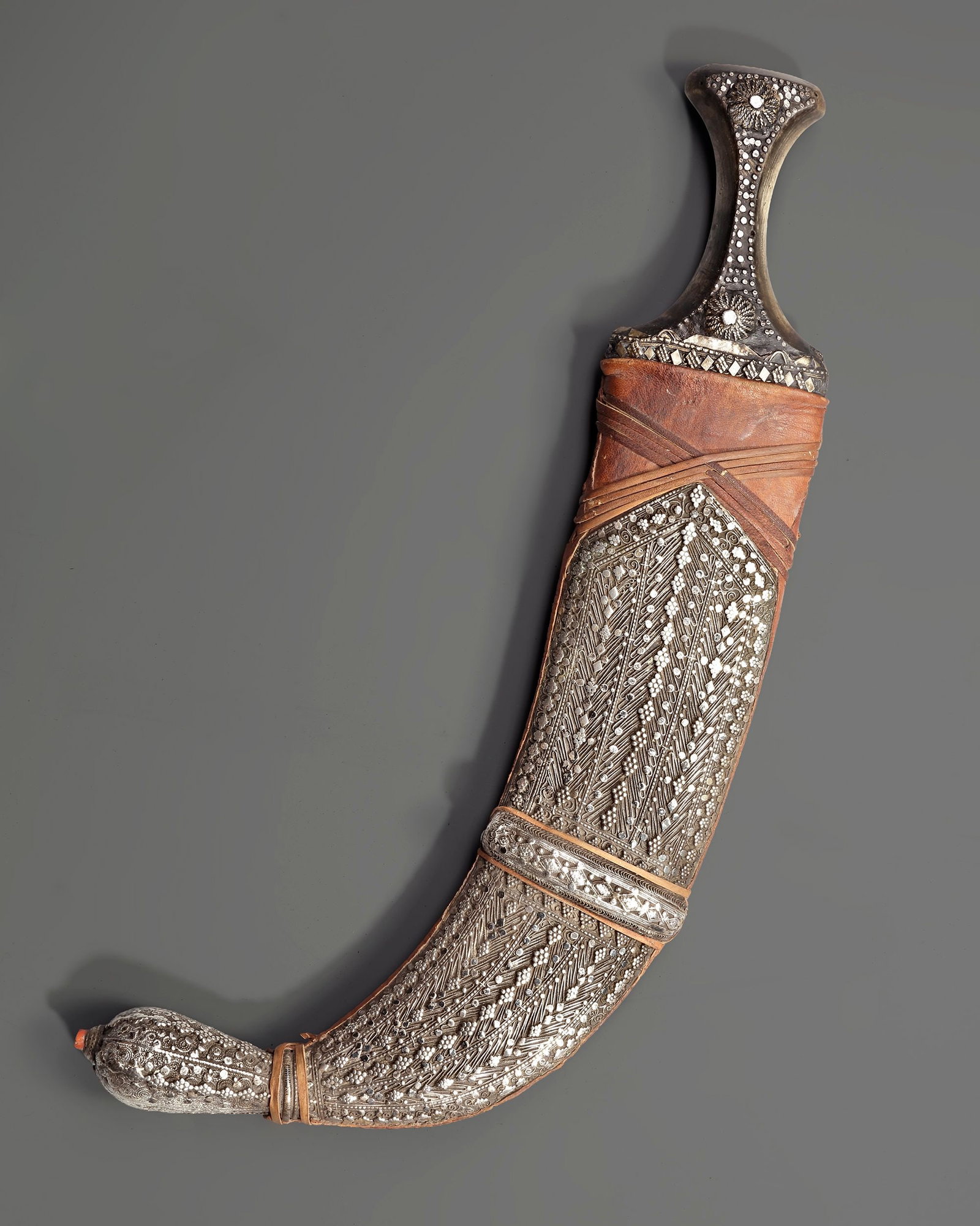A SILVER YEMENI DAGGER, EARLY 20TH CENTURY: A finely crafted Yemeni dagger (jambiya) from the early 20th century, featuring a sharply curved steel blade and a richly decorated silver hilt adorned with traditional granulation and rosette motifs.