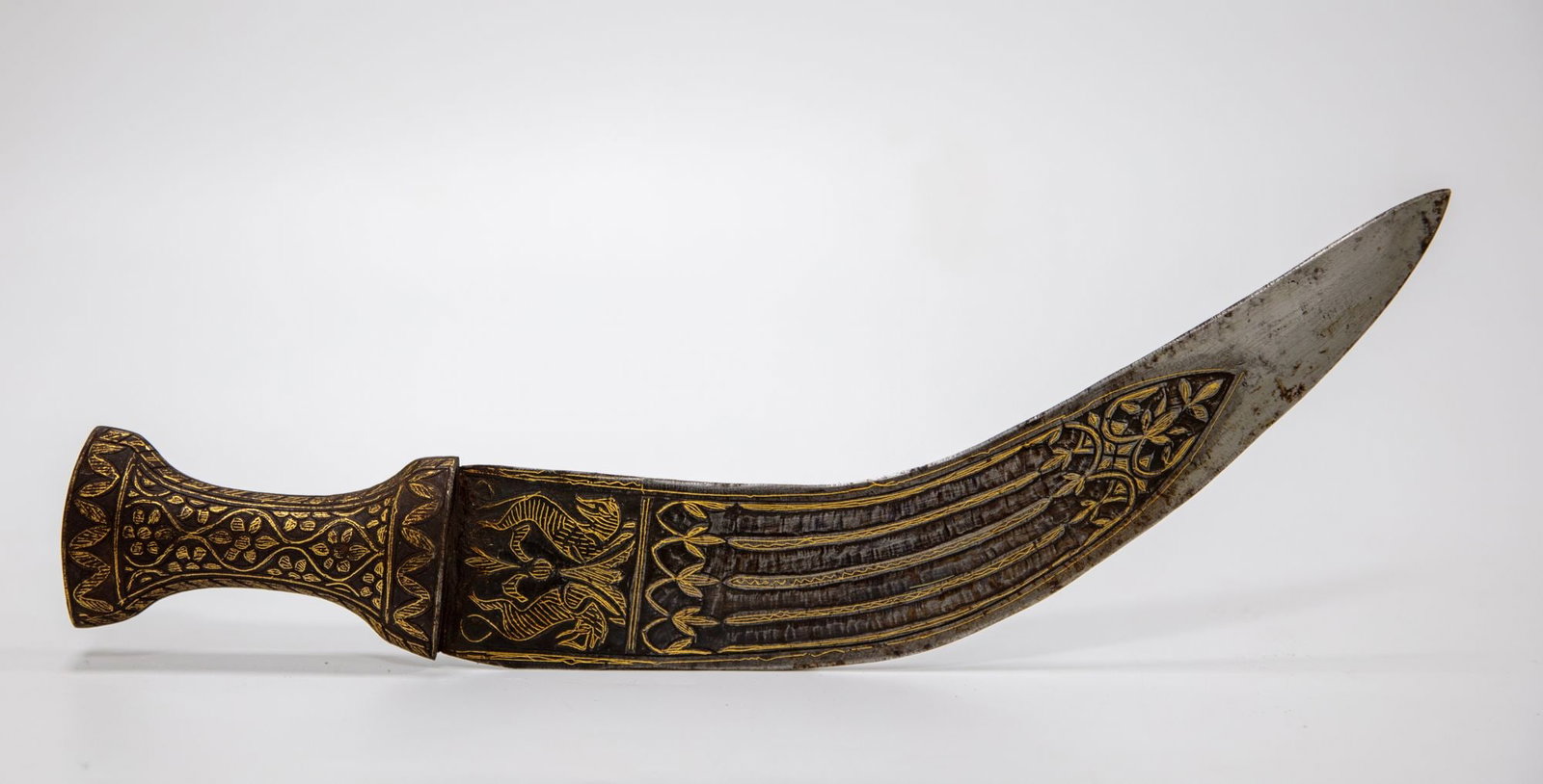 AN INDIAN DAGGER, 19TH CENTURY: A finely made Indian dagger with a strongly curved steel blade, decorated with gold koftgari foliate and geometric motifs along the forte. The grip and guard are richly embellished with dense floral o