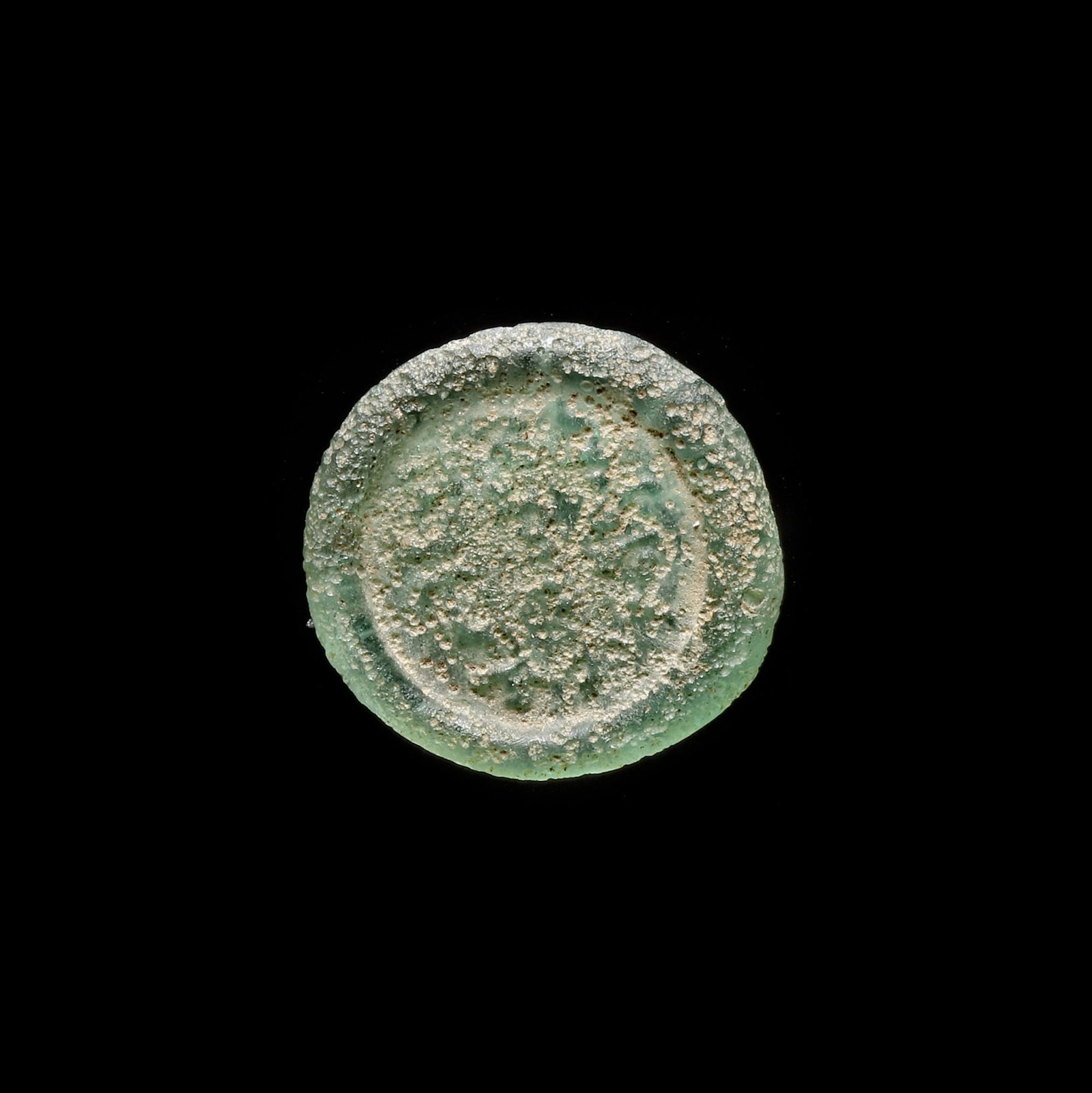 AN EARLY ISLAMIC GLASS WEIGHT OF DIRHAM: Glass weight, moulded and stamped, transparent pale-green in colour, citing in the centre with the name Al-Hakim (386-411 AH/996-1021 AD) 2.776 g., 21 mm. coin weight: 1 dirham.