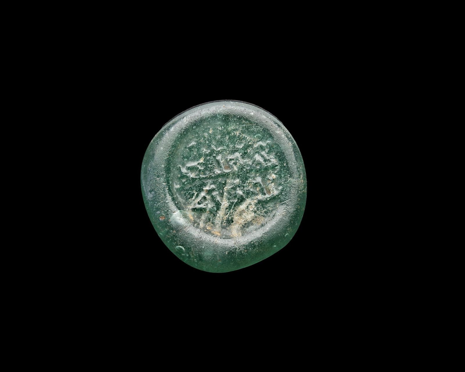 AN EARLY ISLAMIC GLASS WEIGHT OF HALF DIRHAM: Glass weight, moulded and stamped, transparent pale-green in colour, citing in the centre with the name Al-Imam al-Mustansir( 427-487AH/1036-1094 AD). 1.476 g., 16.8 mm. coin weight: half dirham. B 27