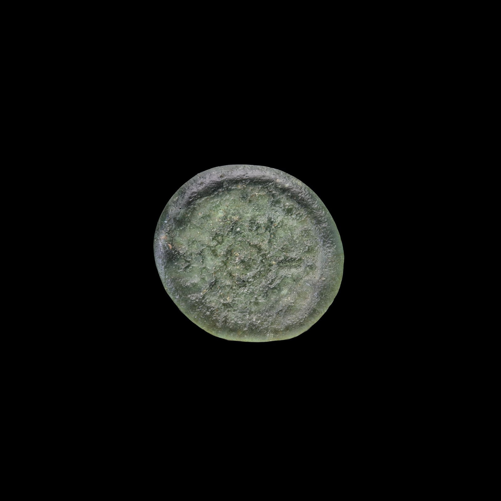 AN EARLY ISLAMIC GLASS WEIGHT OF QUARTER DIRHAM,10TH-11TH CENTURY: Glass weight, moulded and stamped, transparent light-green in colour, citing in the centre with " Adl, Justice". 0.644 g.,13 mm. coin weight: quarter dirham.
