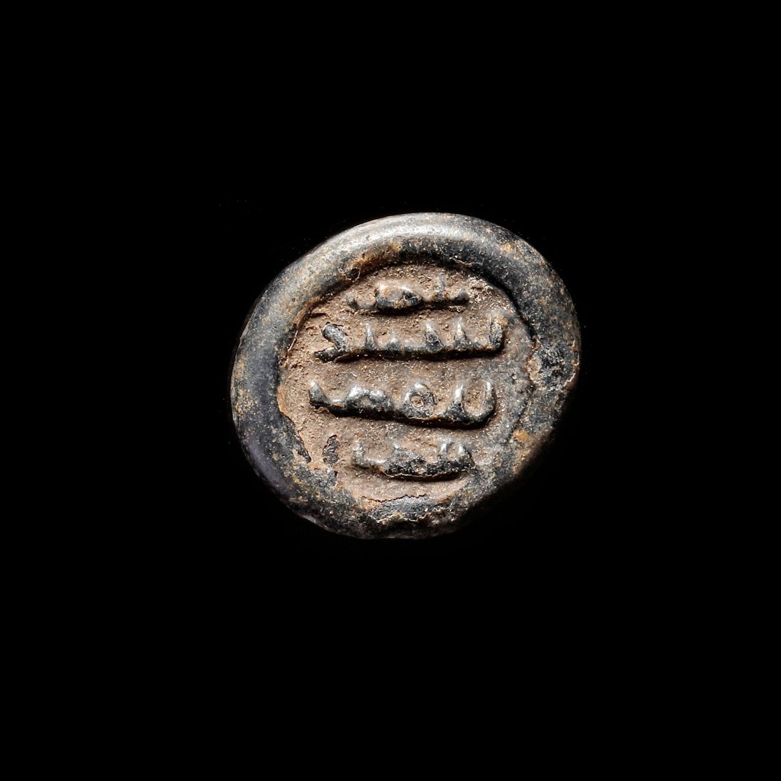 AN EARLY ISLAMIC GLASS WEIGHT OF DIRHAM, 10TH-11TH CENTURY: Glass weight, moulded and stamped, opaque black in colour, citing in the centre with 3 lines of undeciphered Arabic text. 3,046 g., 21,4 mm. coin weight: dirham. B 41