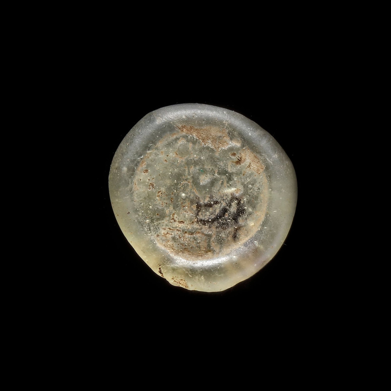 AN EARLY ISLAMIC GLASS WEIGHT OF DIRHAM, 10TH-11TH CENTURY: Glass weight, moulded and stamped, transparent greenish-white in colour, citing in the centre with undeciphered Arabic text. 2.92 g., 19 mm. coin weight: dirham.