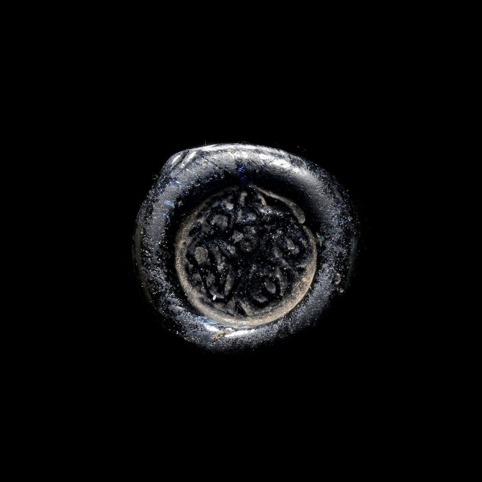 AN EARLY ISLAMIC GLASS WEIGHT OF DOUBLE DIRHAM, 10TH-11TH CENTURY: Glass weight, moulded and stamped, transparent dark-blue in colour, citing in the centre with" Muhammed al-Qahira the year of". 6.077g, 24 mm. coin weight: double dirham.