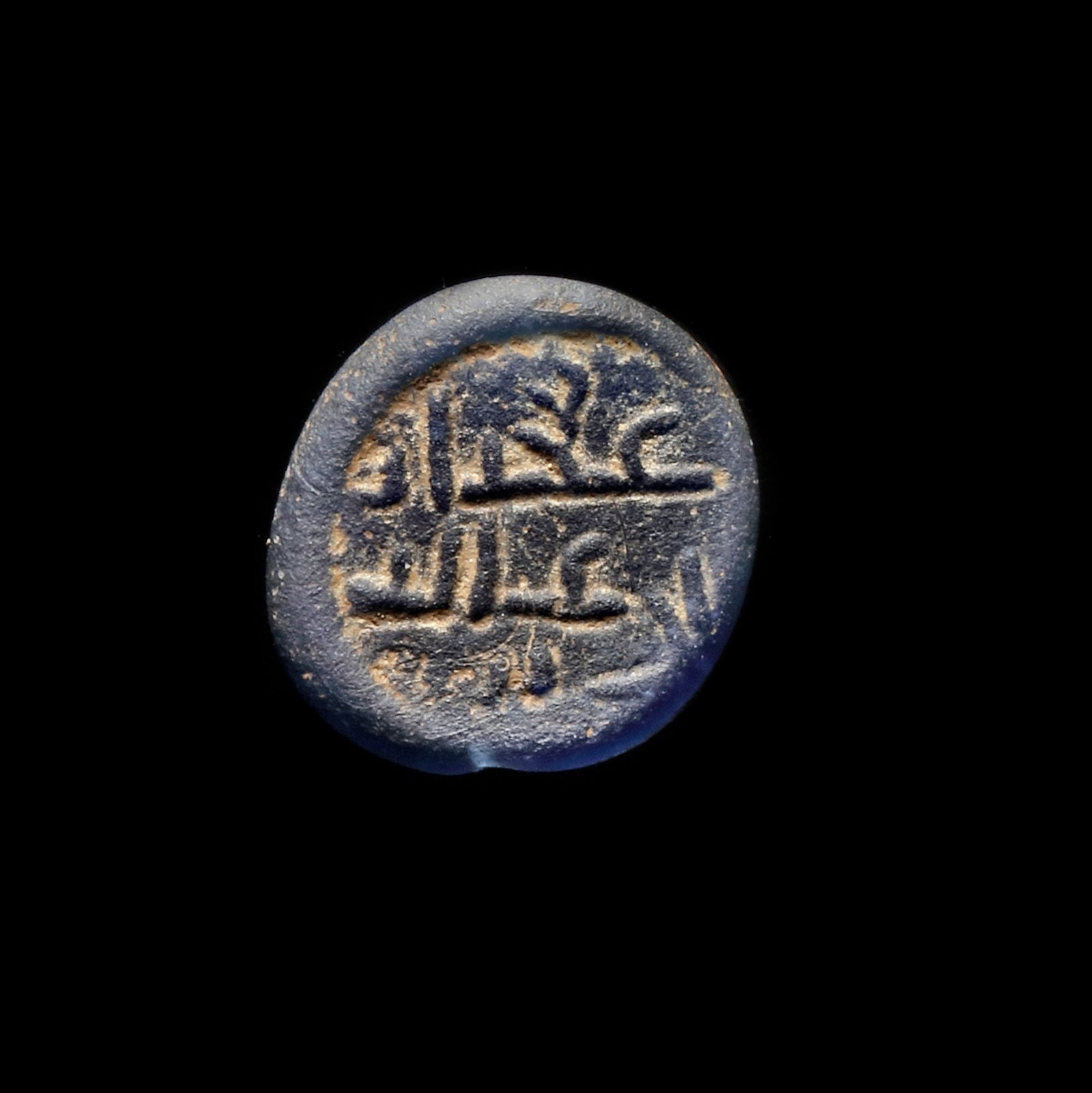 AN EARLY ISLAMIC GLASS WEIGHT OF HALF DIRHAM, 10TH-11TH CENTURY: Glass weight, moulded and stamped, opaque dark-blue in colour, citing in the centre with " Adad Alid". 1.313g, 15 mm. coin weight: half dirham.