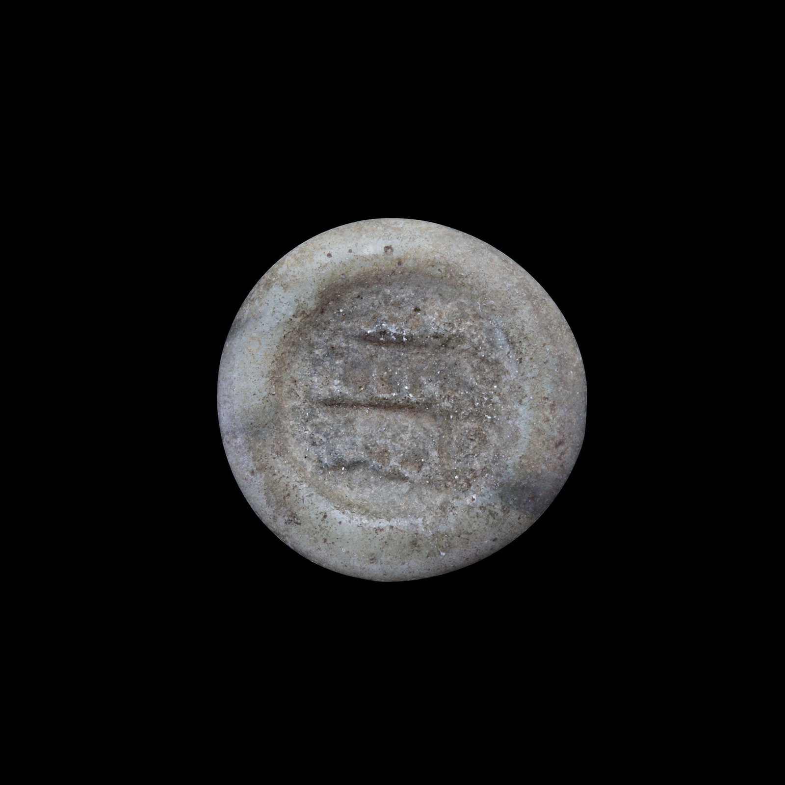 AN EARLY ISLAMIC GLASS WEIGHT OF HALF DIRHAM, 10TH-11TH CENTURY: Glass weight, moulded and stamped, opaque greenish-white in colour, citing in the centre with 3 lines of undeciphered Arabic text. 1.465g, 16.5 mm. coin weight: half dirham.