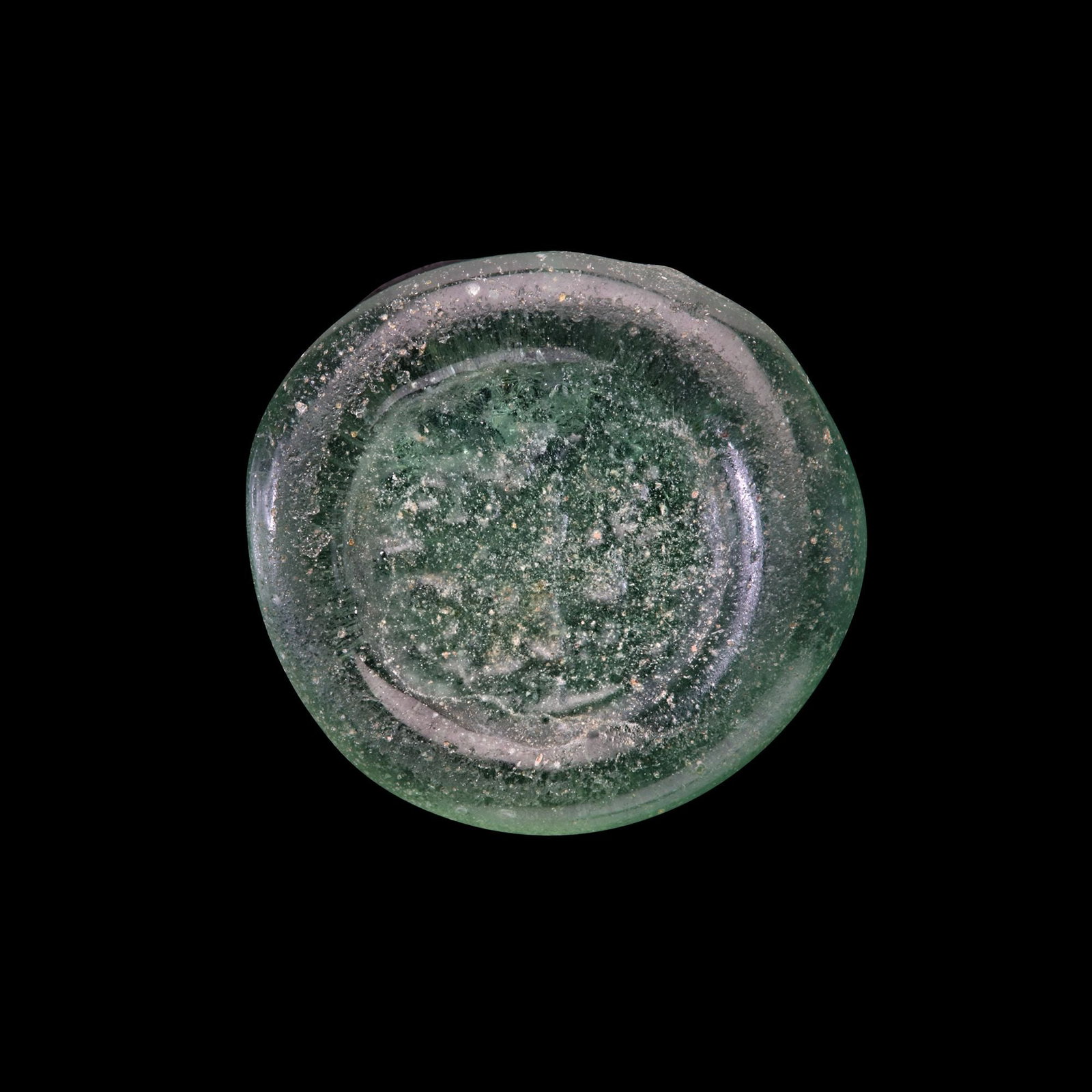 AN EARLY ISLAMIC GLASS WEIGHT OF HALF DIRHAM: Glass weight, moulded and stamped, transparent pale-green in colour, citing in the centre with the name Al-Zahir (412-427 AH/1021-1036 AD). 1.467 g., 14 mm. coin weight: half dirham.