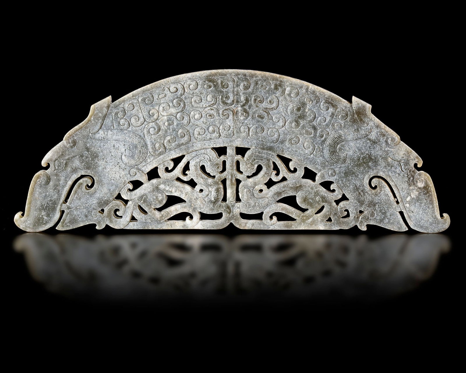 A CHINESE GREEN JADE HUANG WITH DRAGONS, SPRING AND AUTUMN PERIOD (770â€“476 BC): A magnificent green jade huang carved in an elegant arched form and decorated with two opposing dragons. Intricate openwork designs and finely engraved spiral motifs showcase the refinement and symbol