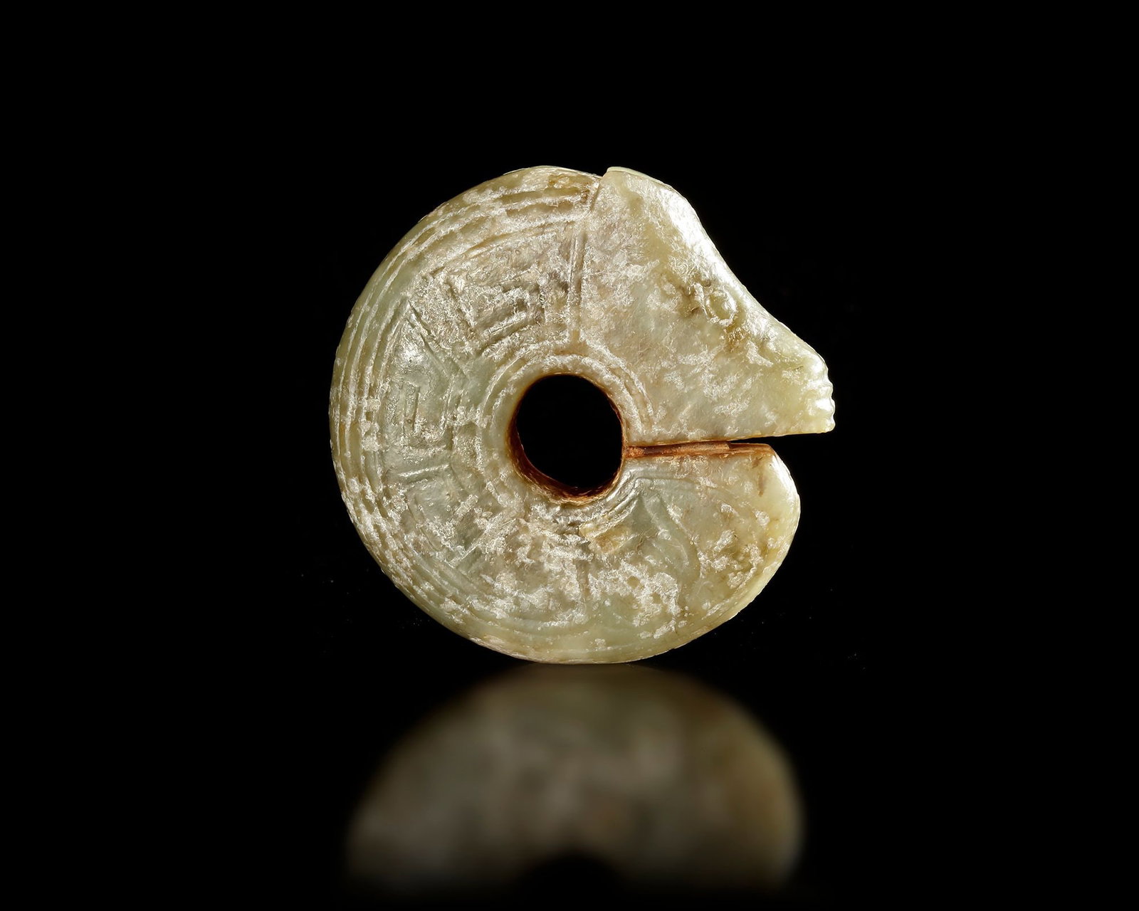 A JADE DRAGON, DRAGON, SHANG DYNASTY ( 1600â€“1046 BC): A finely carved jade dragon pendant . The piece is formed in a circular, coiled dragon shape with a central perforation and a stylized dragon head. Subtle carved patterns The jade displays a soft, pal