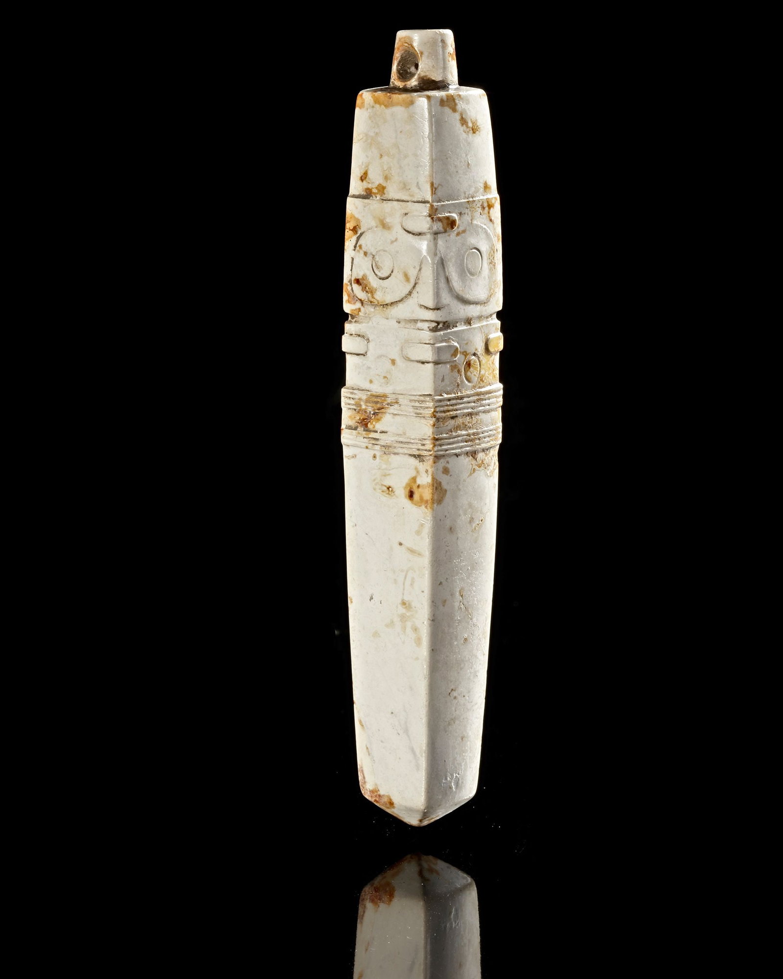 A JADE PENDANT NEOLITHIC PERIOD, CHINA (CIRCA 3300â€“2300 BC): Four-sided pendant carved from white jade, featuring stylized mask motifs and geometric bands typical of Liangzhu ritual art. The piece shows natural mineral inclusions and surface patina consistent w