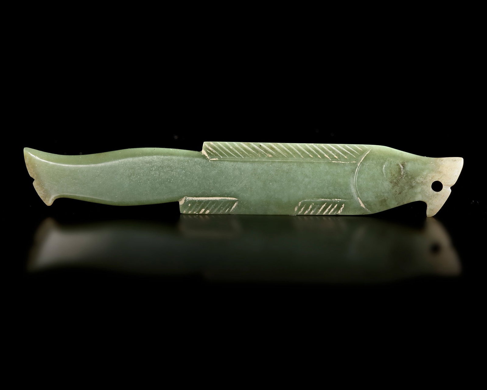 A GREEN JADE FISH PENDANT, SHANG DYNASTY (CIRCA 1600â€“1046 BC): A finely carved green jade pendant in the form of a stylized fish, The elongated body is decorated with incised lines suggesting fins and scales, while the head is carefully detailed with a drilled ey