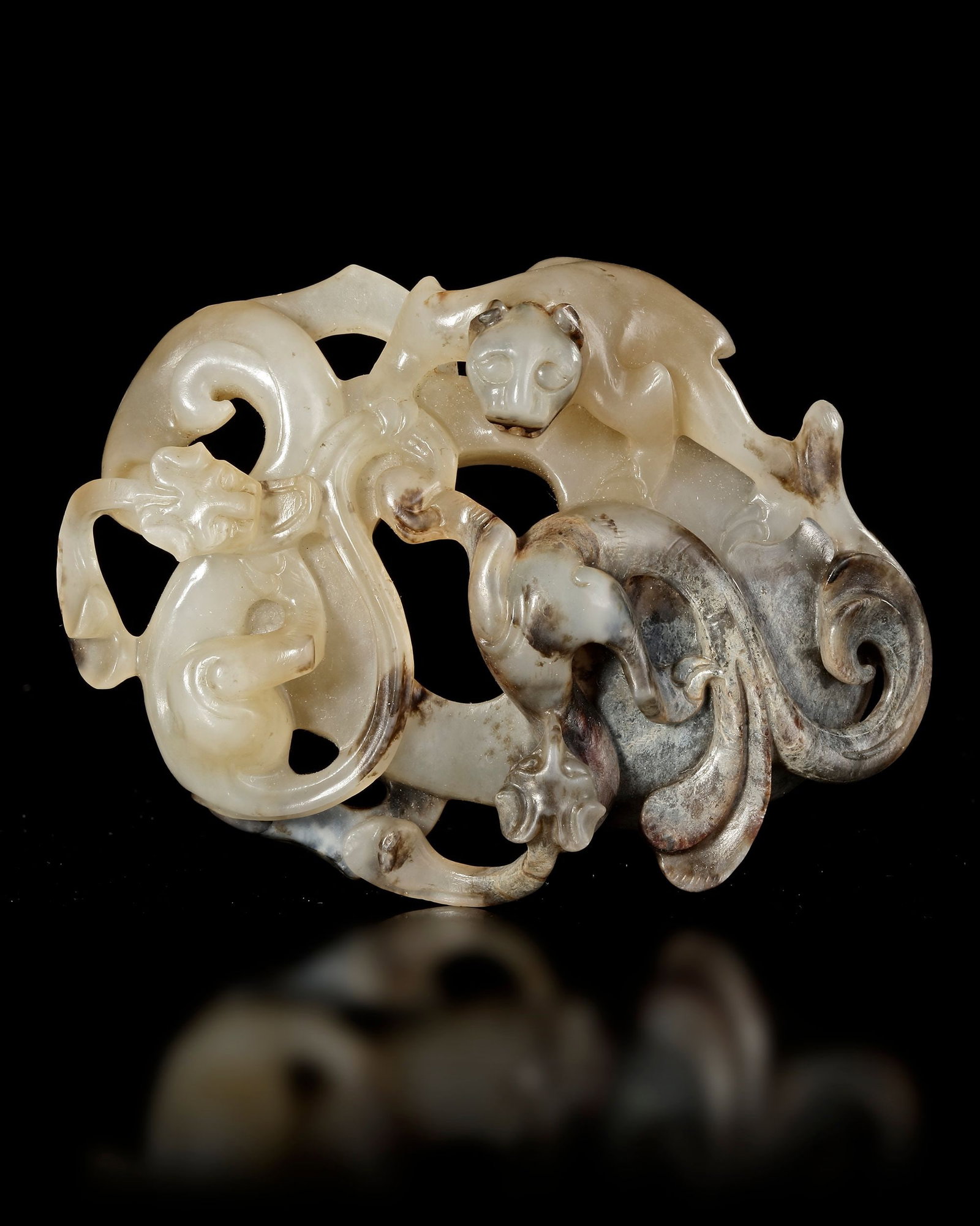 A JADE PENDANT, HAN DYNASTY (220 ADâ€“220 AD): A finely carved jade pendant featuring an openwork composition with stylized mythical animals and flowing ornamental forms. The stone shows natural color variations and mineral inclusions, enhancing i