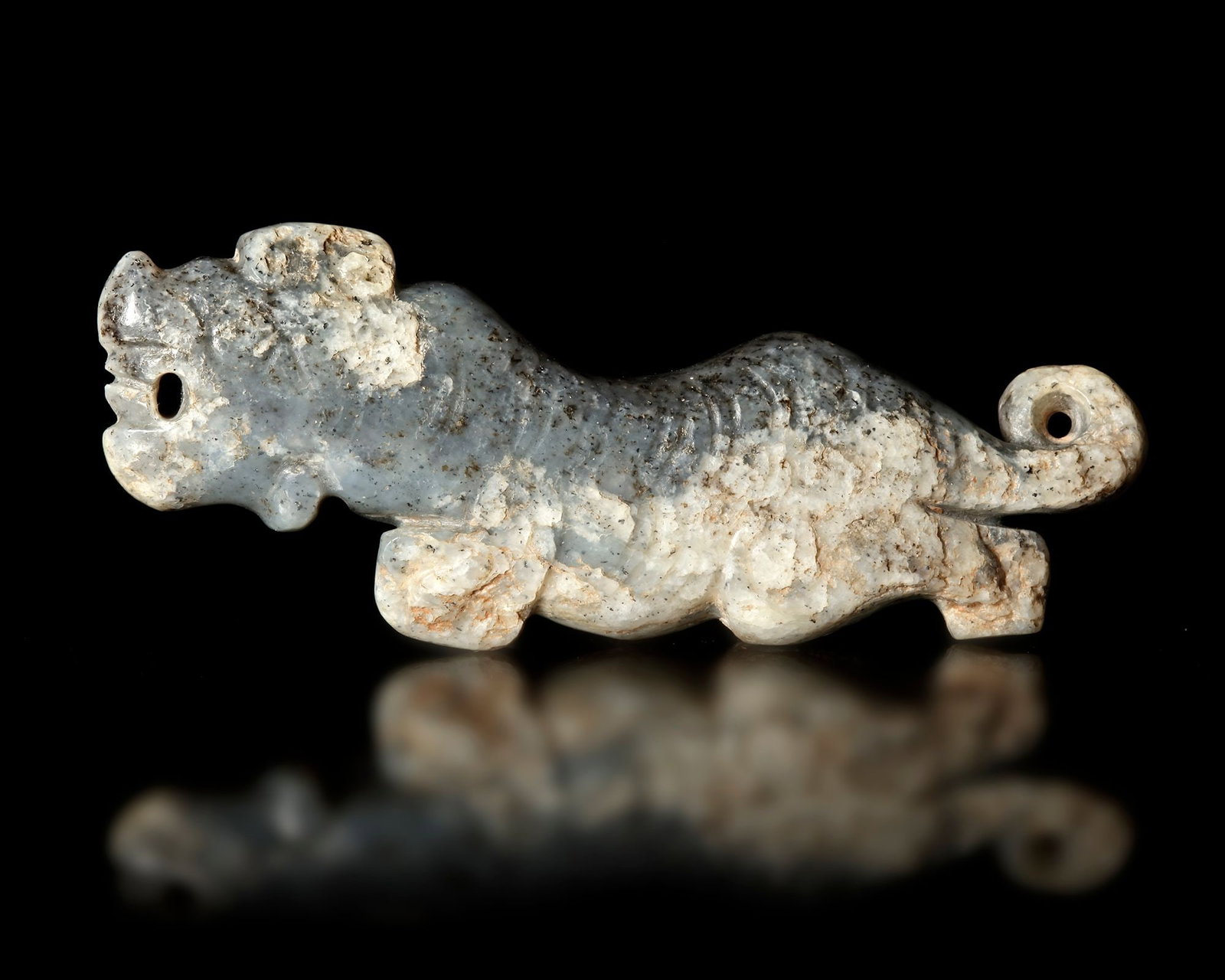 A JADE TIGER, CHINA, SHANG DYNASTY (c. 1600â€“1046 BCE): Ancient Chinese tiger carved from grey jade, (c. 1600â€“1046 BCE). The stylized animal is depicted in a dynamic, elongated form with a curled tail and drilled eye openings, likely intended for