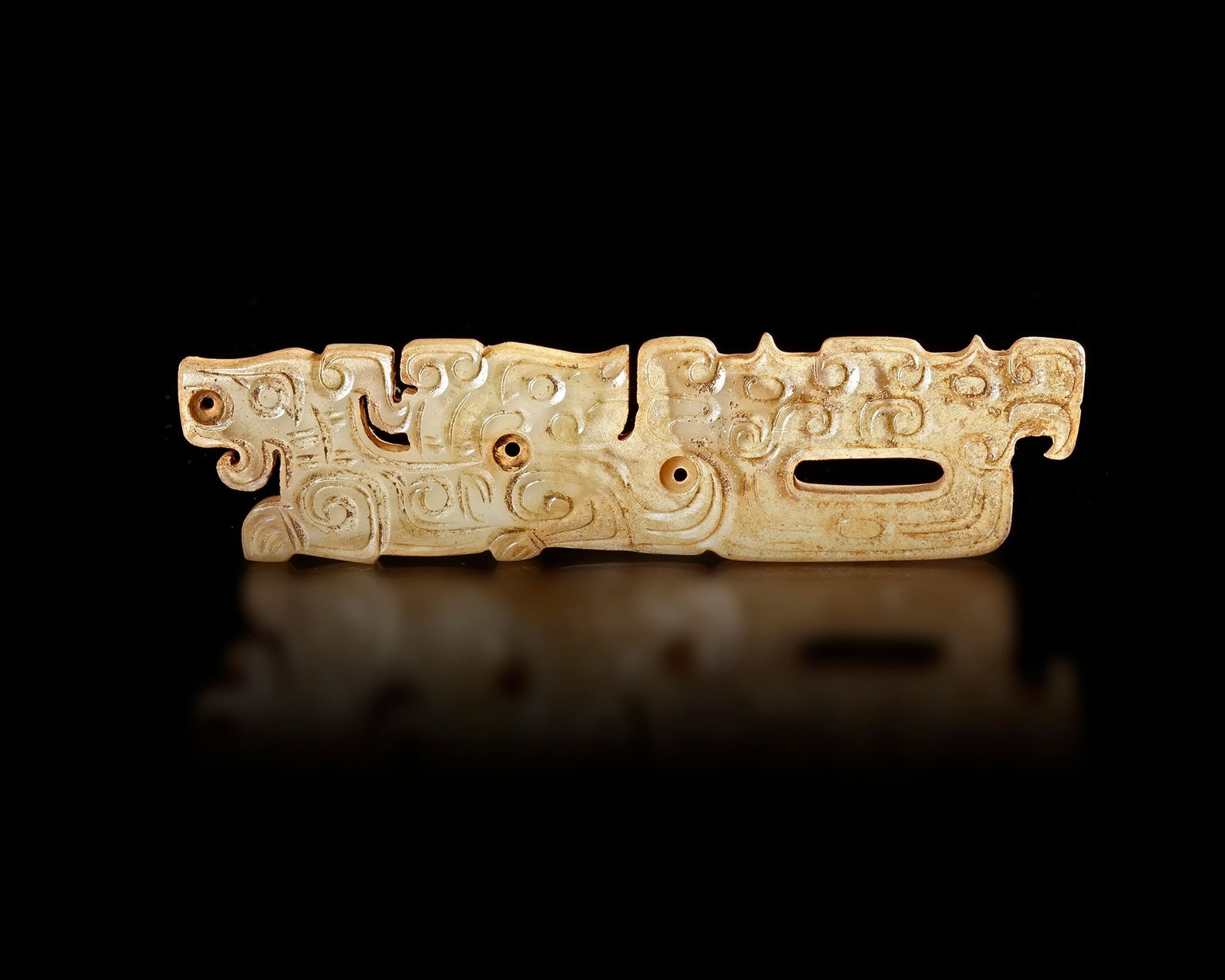 A JADE PENDANT, CHINA, ZHOU DYNASTY, (c. 1046â€“256 BC): A finely carved jade pendant .The elongated plaque is decorated with stylized animal and scroll motifs,The jade shows a soft natural tone with subtle surface patina developed over centuries. Size: 9.2