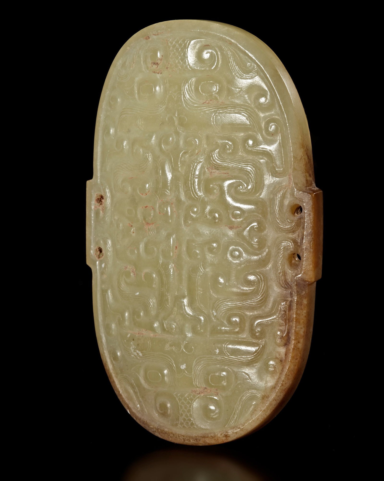 A CURVED YELLOW JADE ORNAMENT, HAN DYNASTY (206 BC â€“ 220 AD): A finely carved curved yellow jade ornament . The oval plaque is decorated with symmetrical archaic scroll and mask-like motifs, reflecting the influence of earlier bronze ritual designs often reprodu