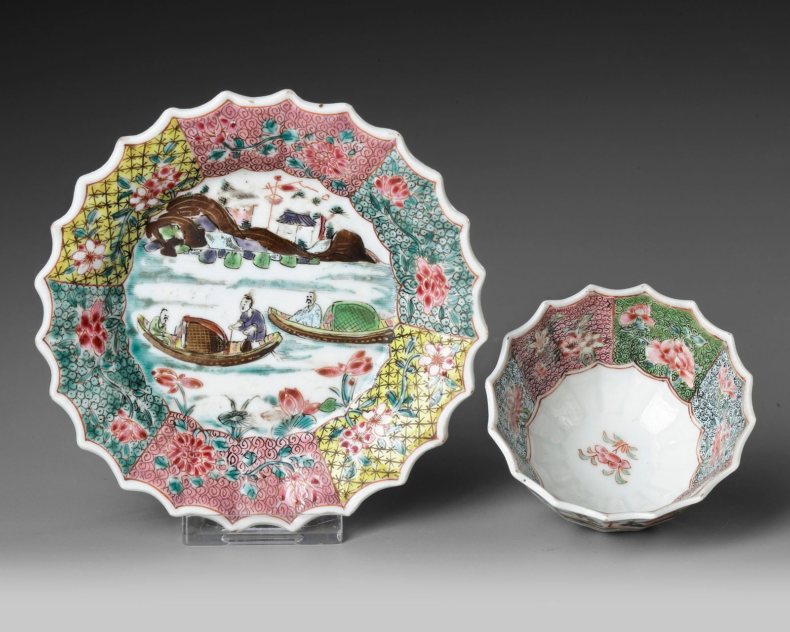 a CHINESE FAMILLE ROSE CHRYSANTHEMUM-FORM CUP AND SAUCER, EARLY QIANLONG PERIOD (1735-1795): A finely painted Chinese Famille Rose chrysanthemum-form cup and saucer . Decorated with a charming riverside landscape featuring figures in boats, pavilions, and mountains, framed by vibrant floral a