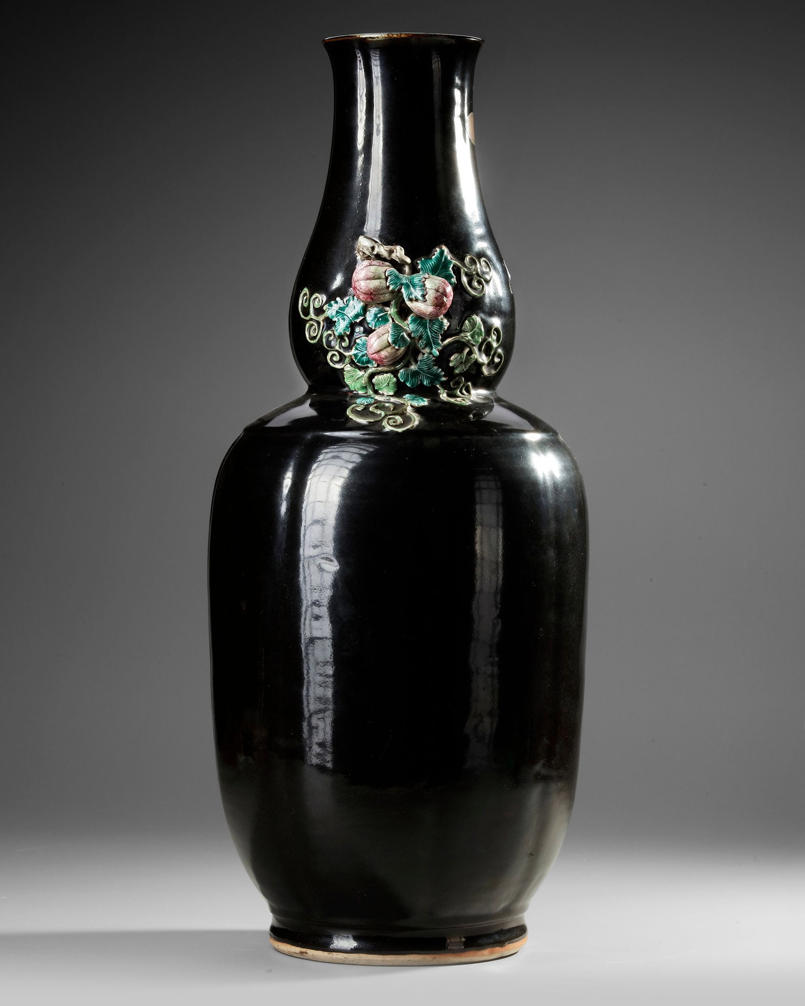 A RARE FAMILLE ROSE-DECORATED MIRROR-BLACK-GLAZED DOUBLE-GOURD VASE, CHINA, 18TH CENTURY: The neck is flanked by a pair of handles formed by vines bearing three gourds in high relief amidst the leafy tendrils that trail down onto the shoulder, all against the lustrous black ground. The int
