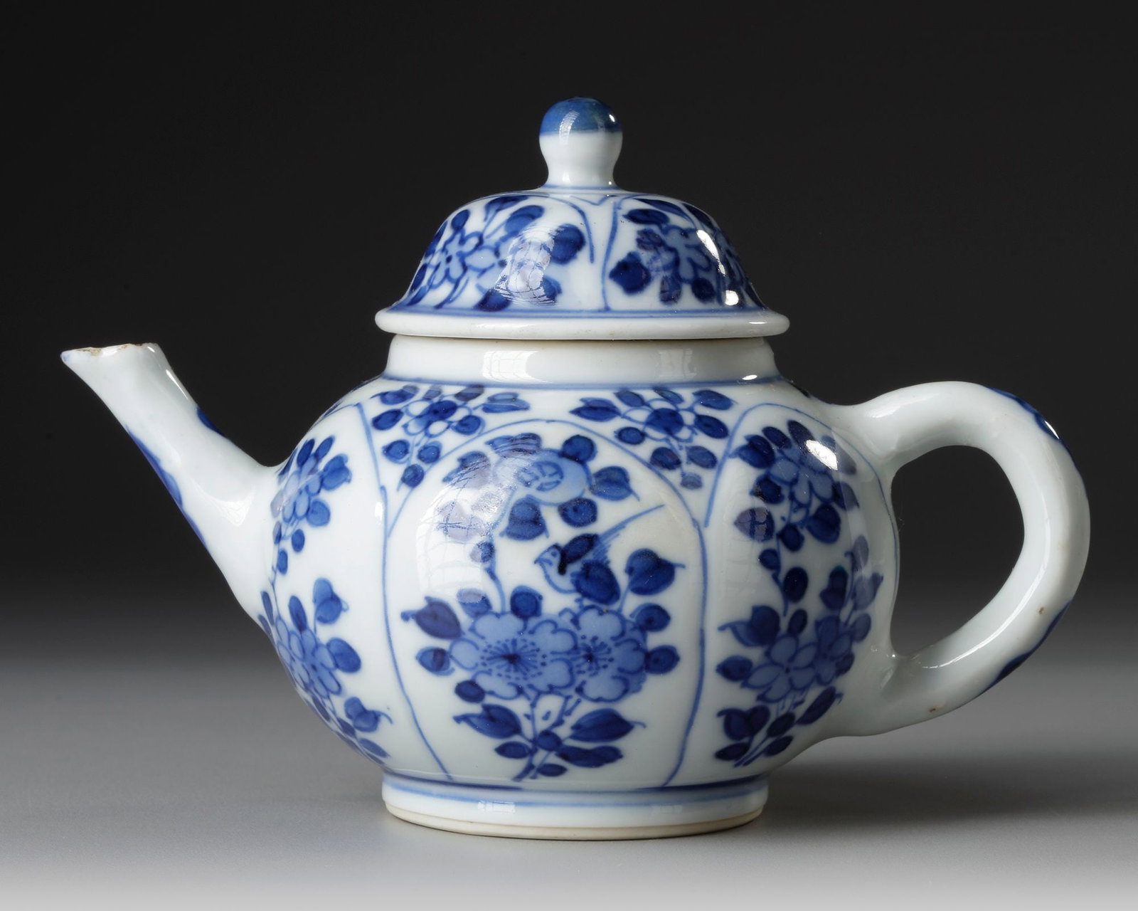 A CHINESE TEAPOT, KANGXI PERIOD (1662â€“1722): Elegant Chinese blue and white porcelain teapot, decorated with six floral panels in underglaze cobalt blue. The rounded body is finely painted with blossoming flowers and leafy scrolls, framed within