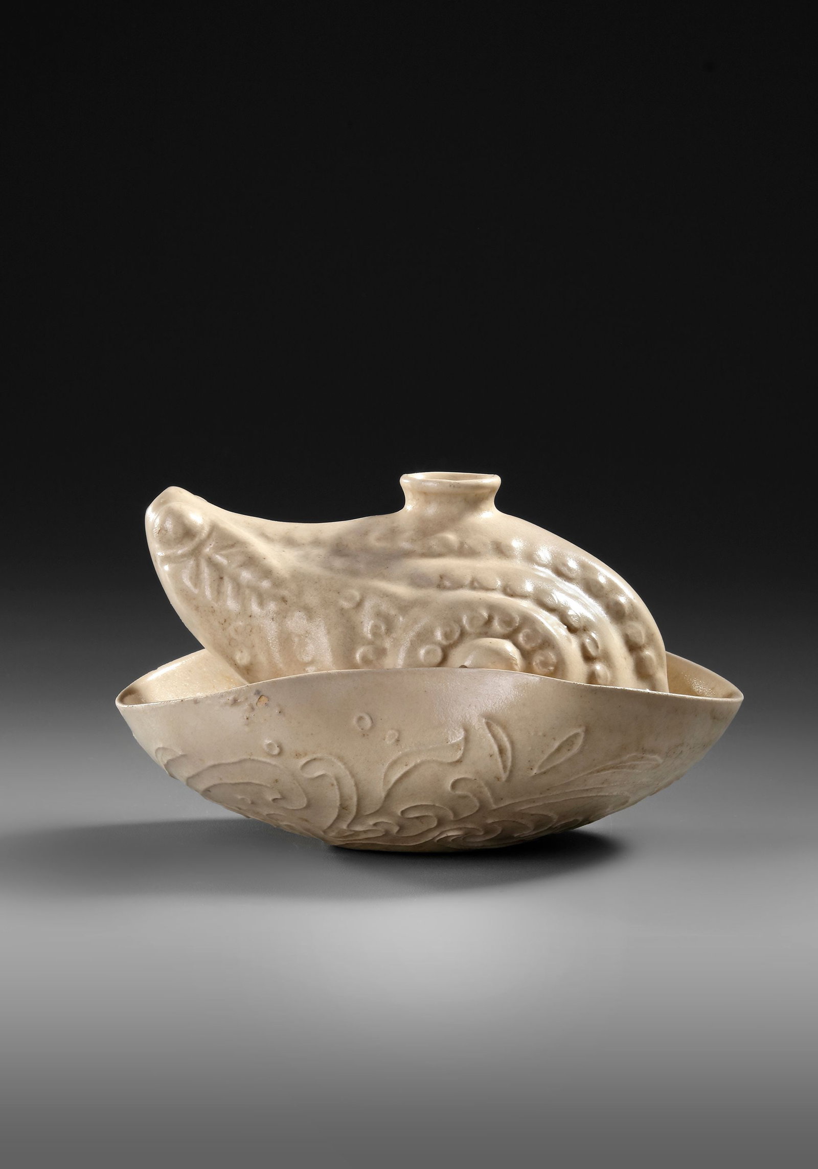 A CHINESE WHITE GLAZED FROG-FORM WATER DROPPER, MING DYNASTY (1368â€“1644): The large water dropper is moulded in the shape of a crouching frog with a circular aperture on its back and a short spout issuing from its mouth, seated on an attached bowl carved with floral leafy s