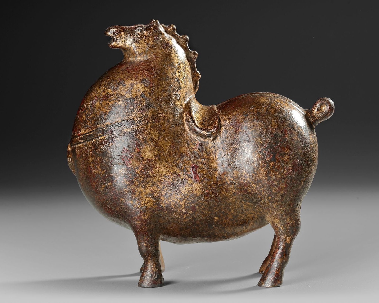 A CHINESE GILT BRONZE HORSE STATUE,19TH CENTURY: A Chinese cast bronze horse features a rounded, exaggerated form with a pronounced mane, detailed saddle, and small yet sturdy legs with traces of gilding. 17 by 17 by 9 cm.